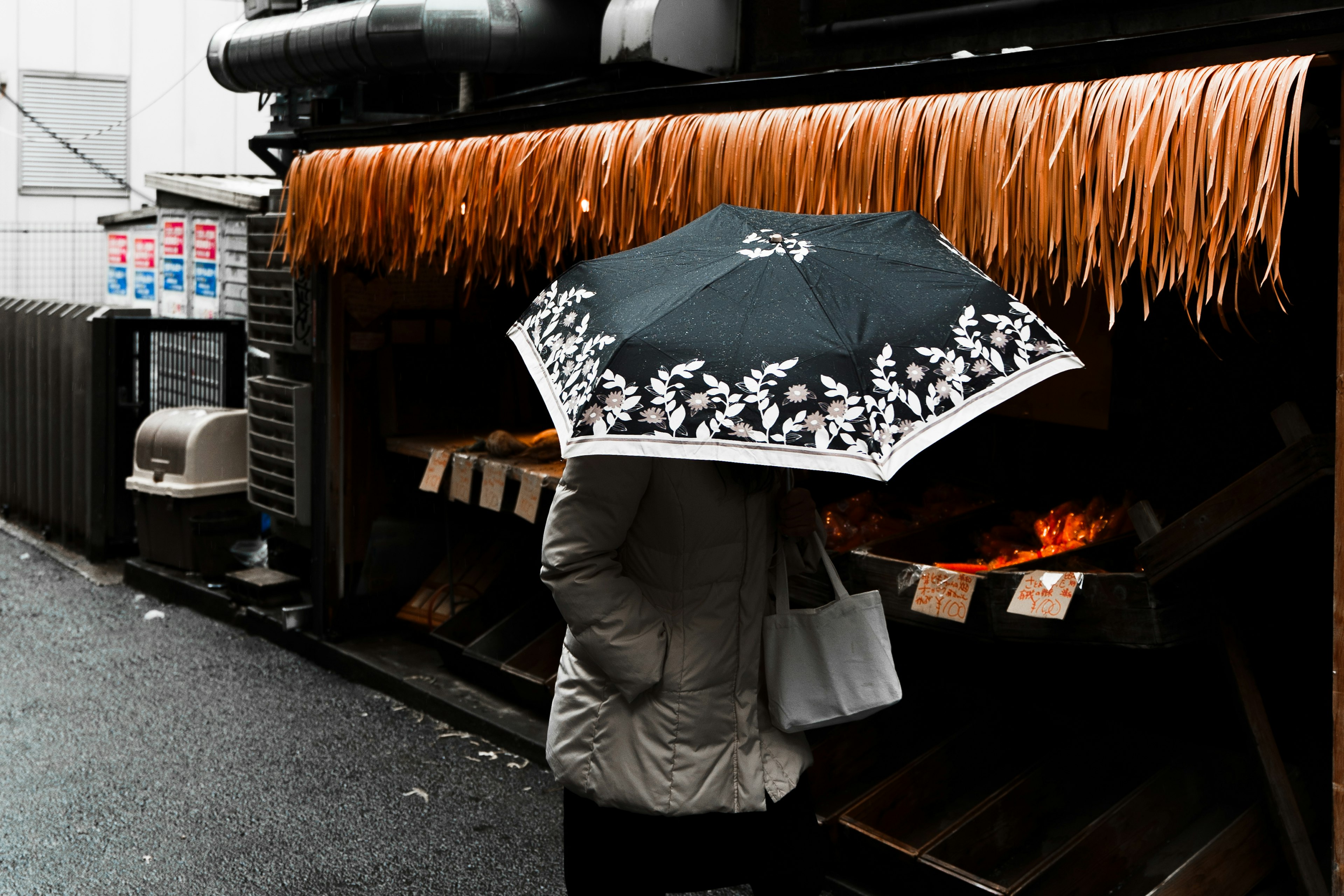 A person holding an umbrella standing in front of a food stall on a rainy day