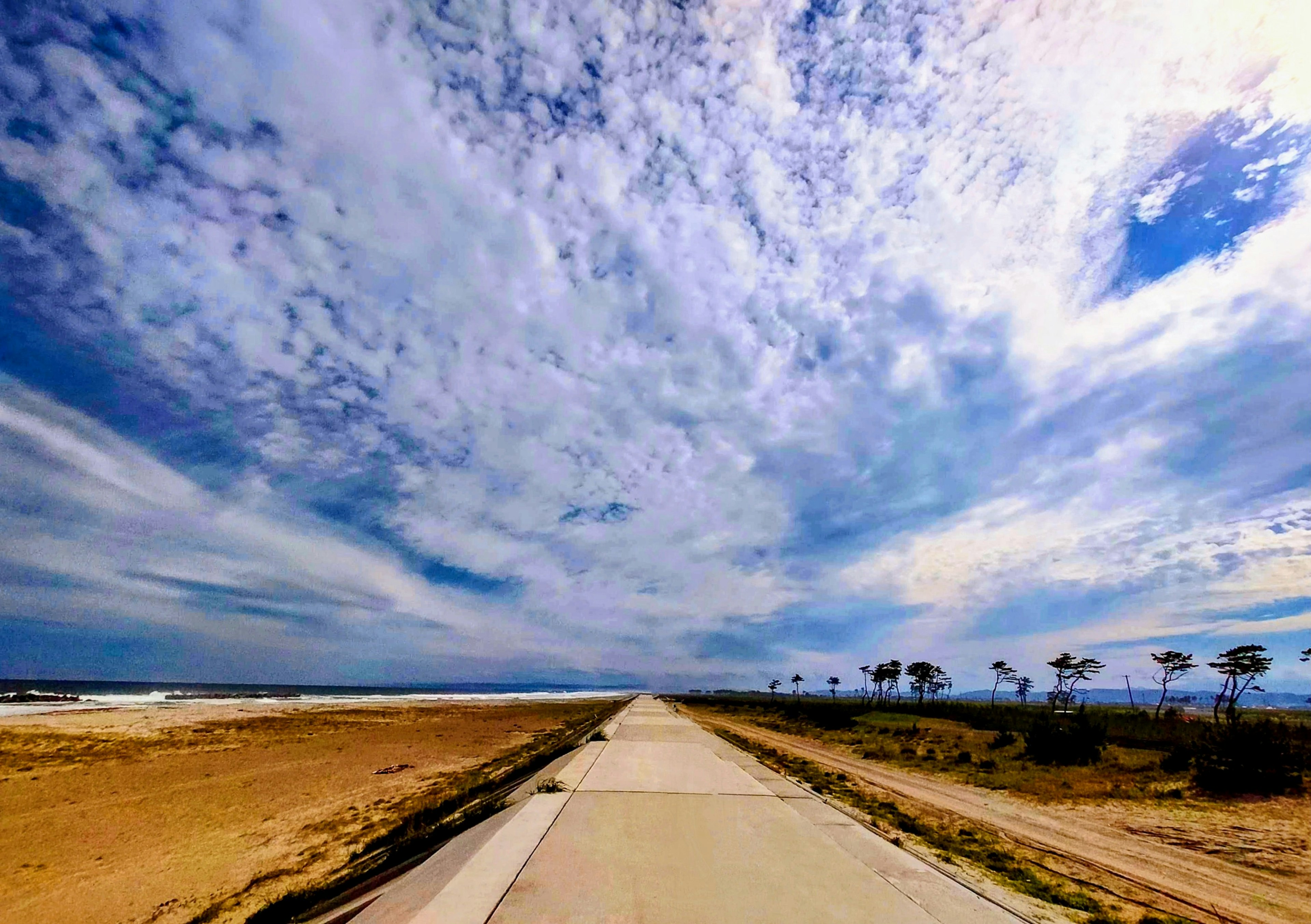 Eine lange Straße, die zu einem weiten Himmel mit verstreuten Wolken führt