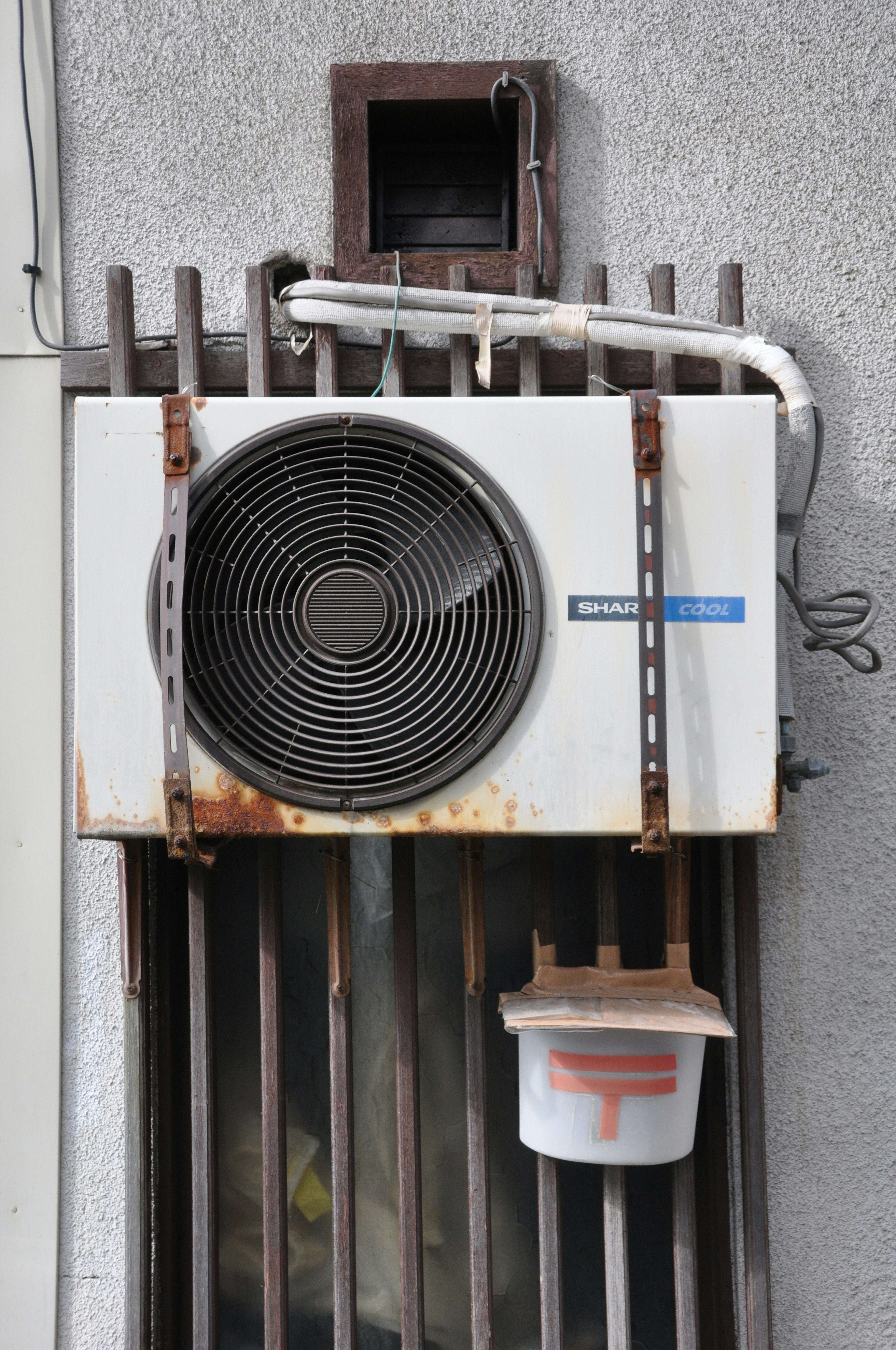 Image of an old air conditioner mounted on a wall showing rusted metal and piping