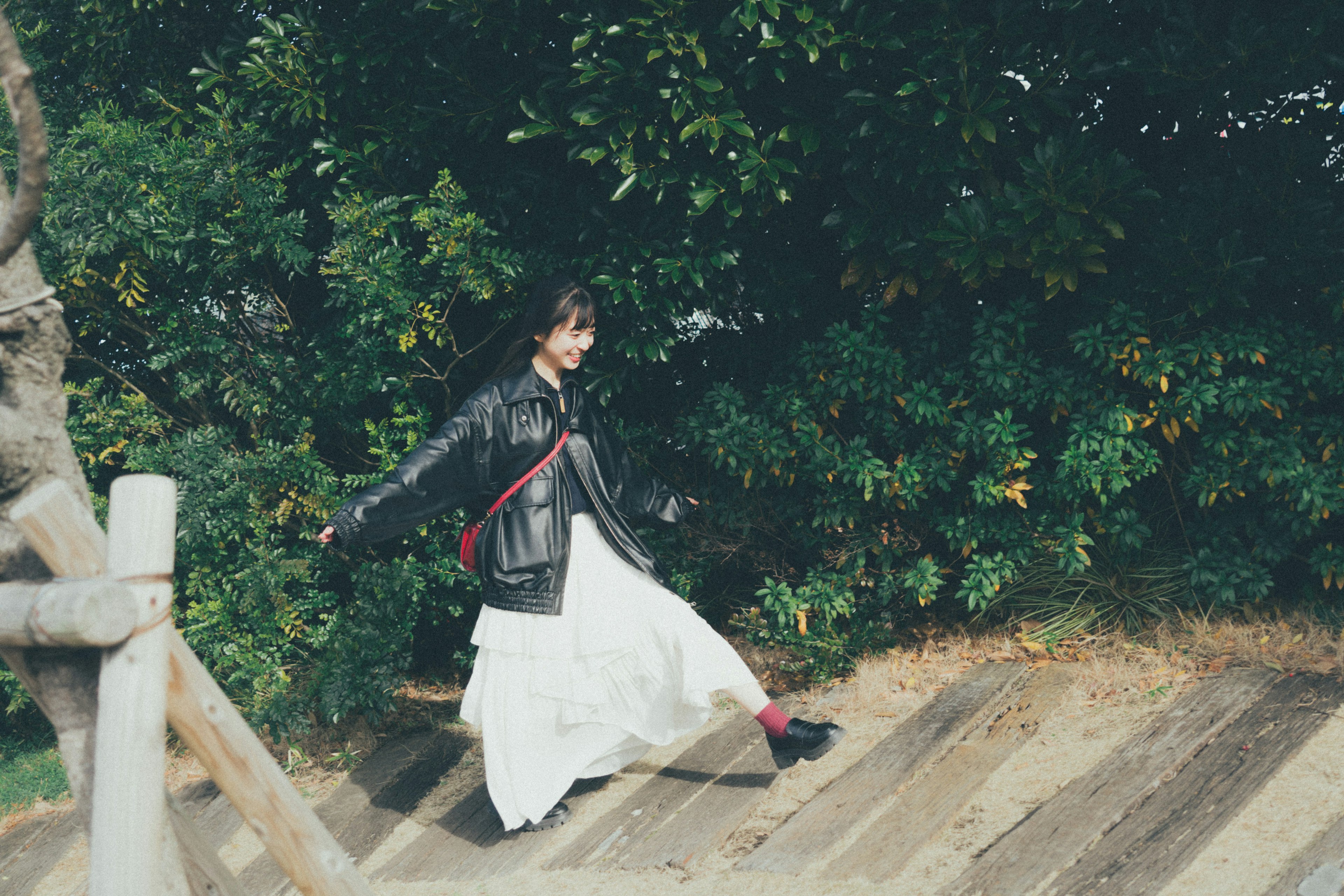 Woman walking between trees wearing a black jacket and white dress