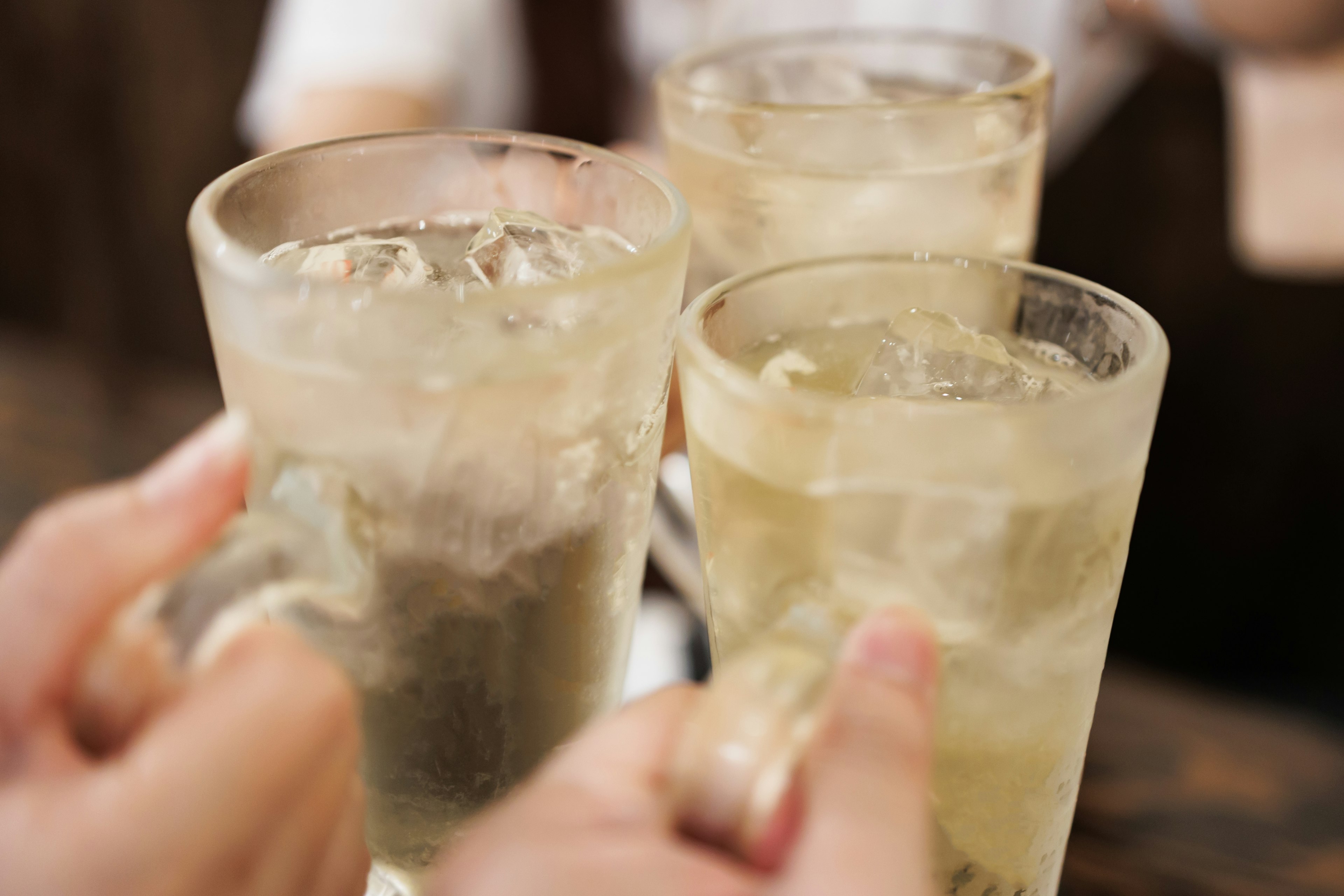 Tres vasos llenos de hielo y una bebida clara chocando en un brindis