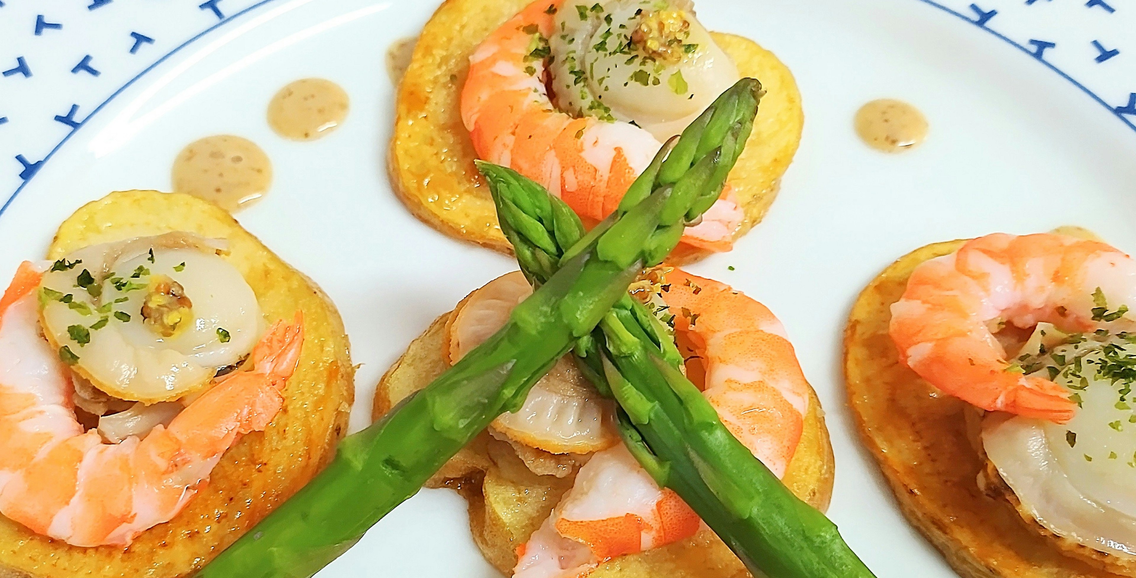 Appetizer featuring shrimp and scallops arranged on a plate with crossed asparagus