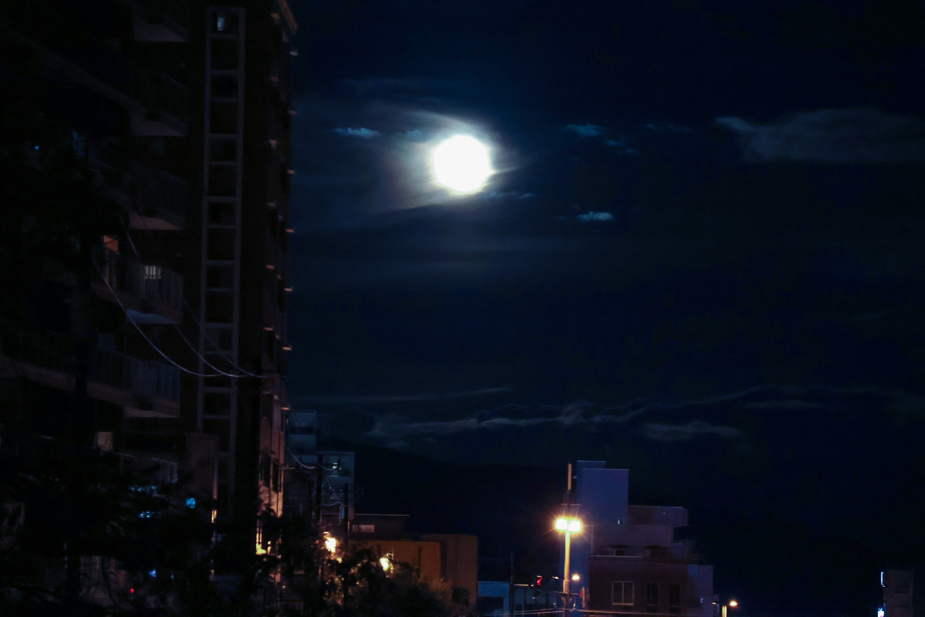 Paesaggio urbano notturno con luna piena luminosa e nuvole scure