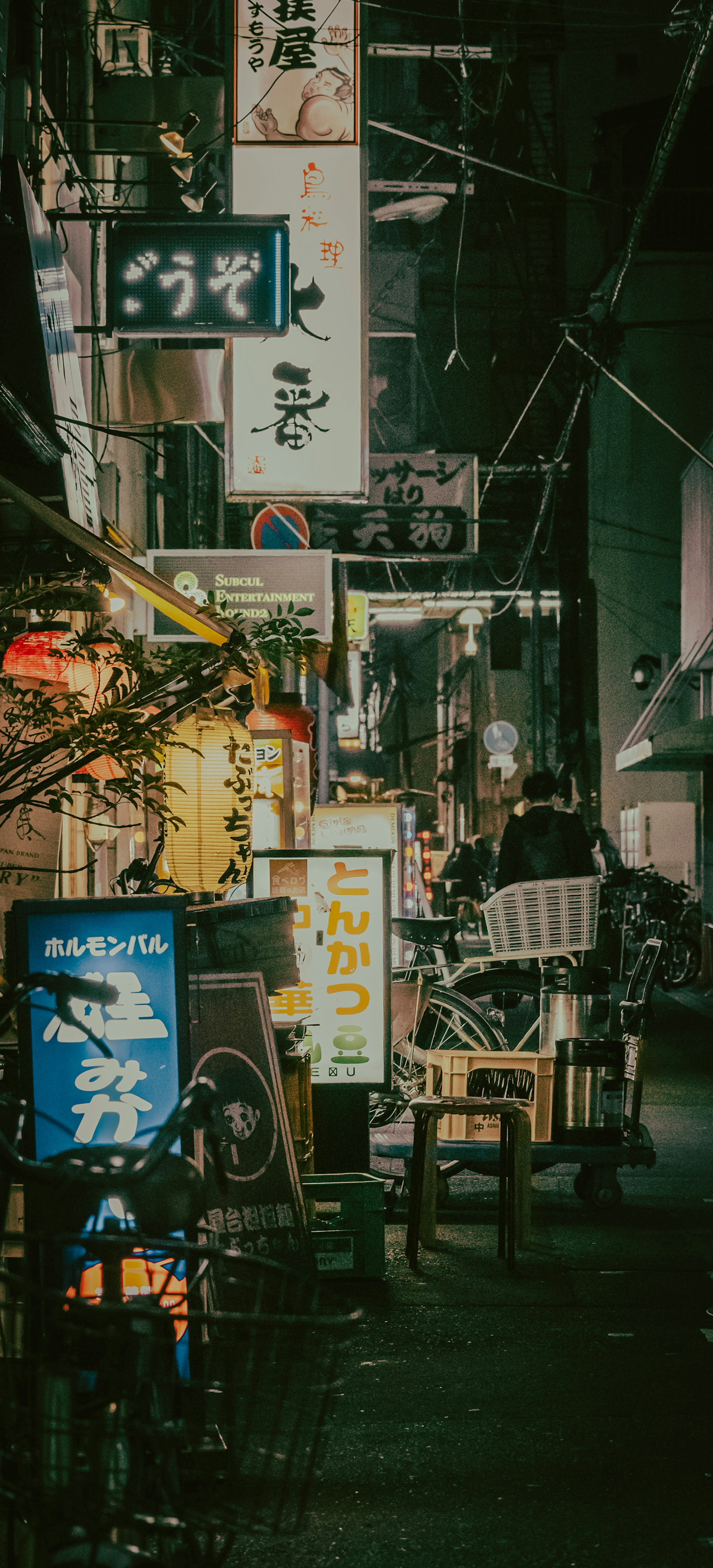 Illuminated restaurant signs line a narrow street in a Japanese city at night