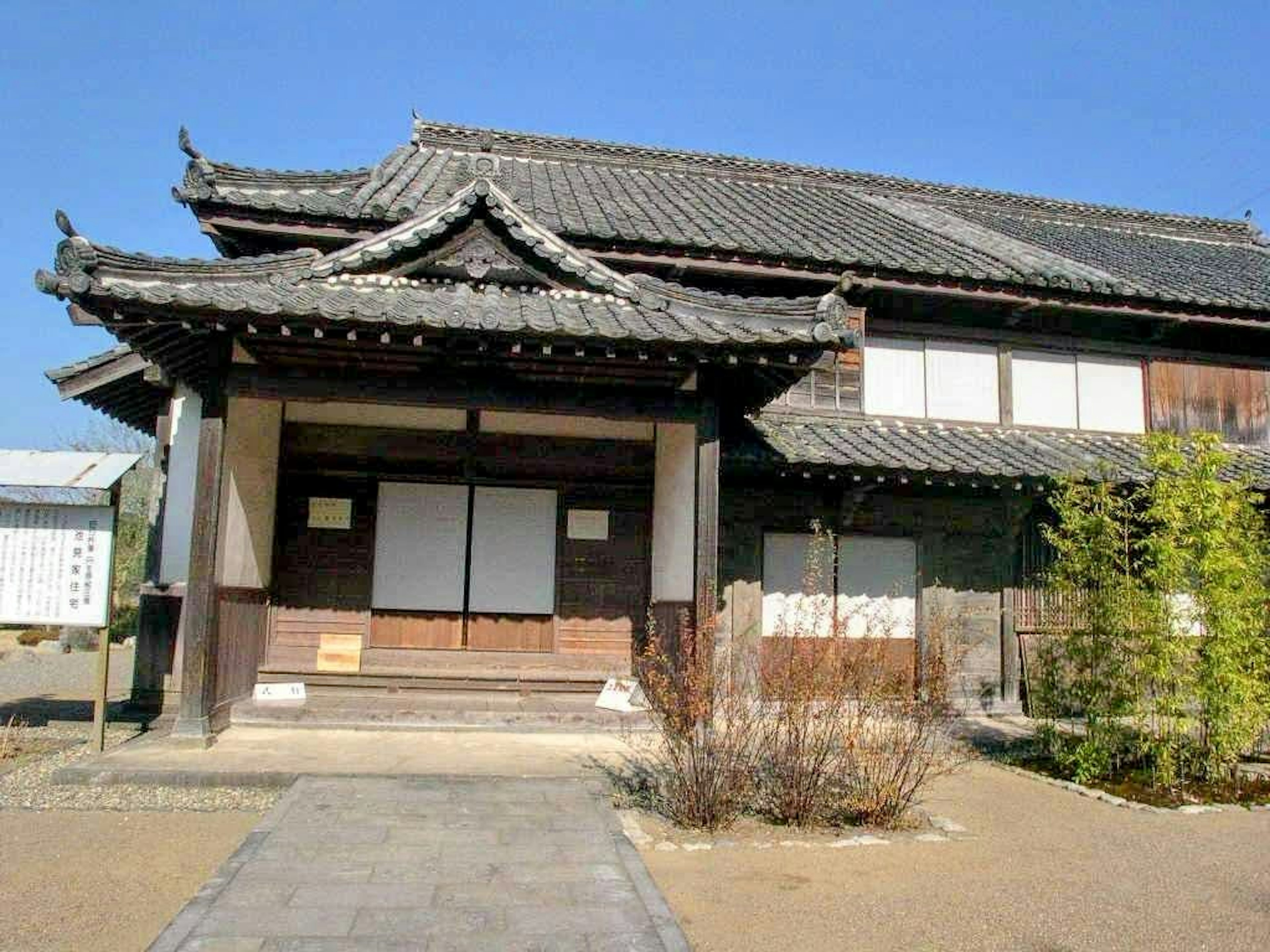 Extérieur d'une maison japonaise traditionnelle avec toit en tuiles et structure en bois, bambou dans le jardin