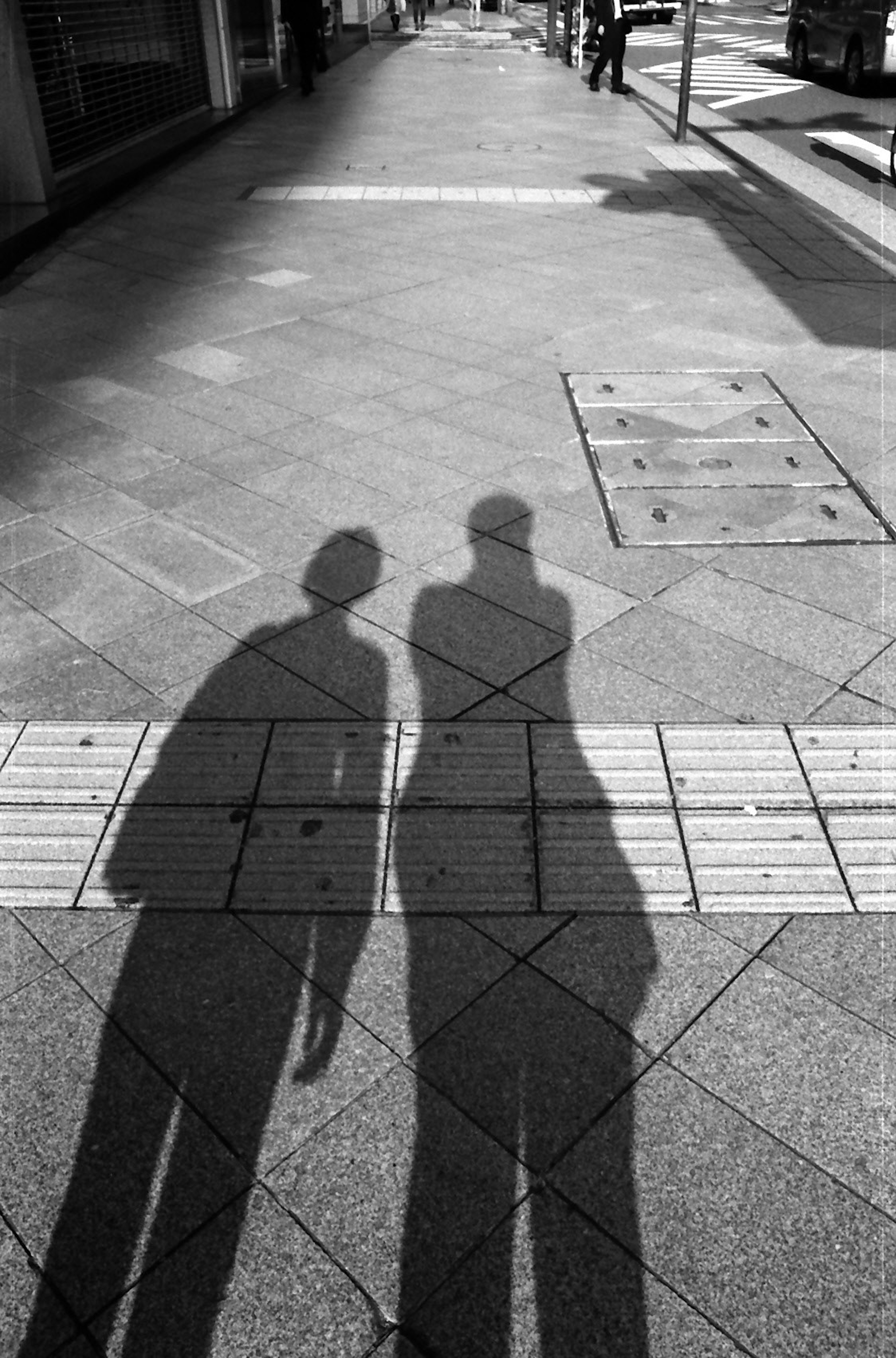 Silhouettes de deux personnes projetant des ombres sur un trottoir de la ville