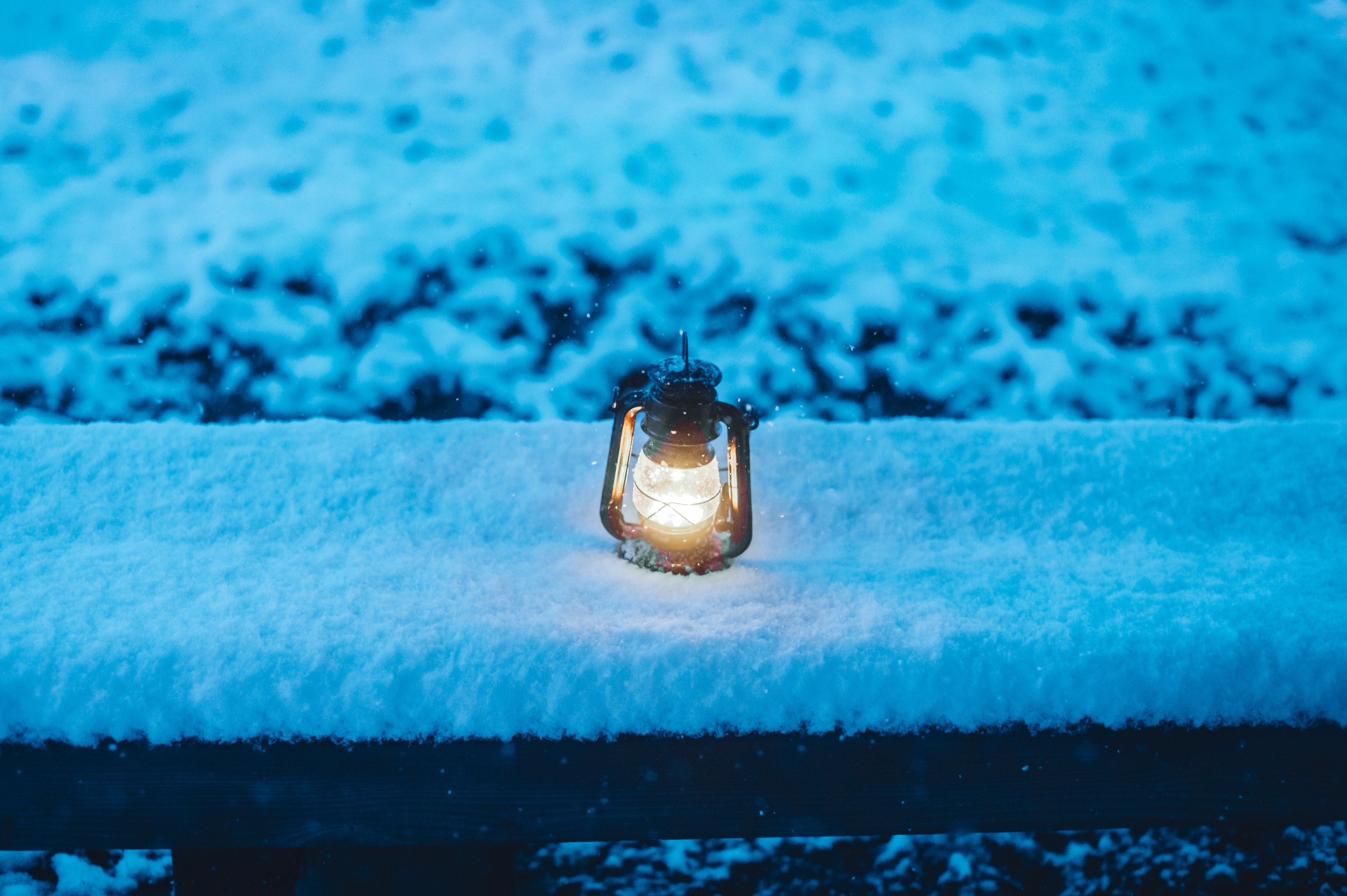 A lantern emitting warm light placed on a snow-covered wooden bench