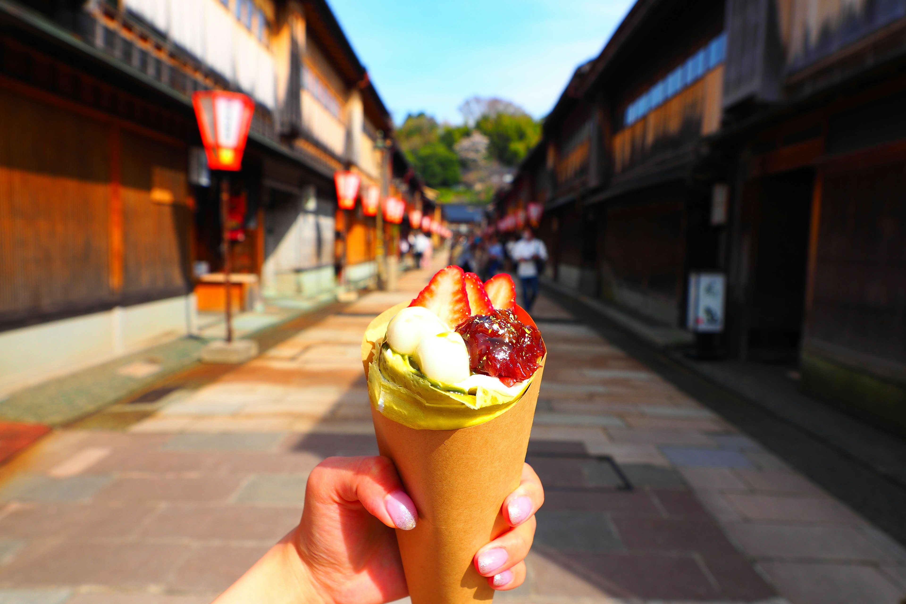 Hand holding green tea ice cream with traditional street in the background