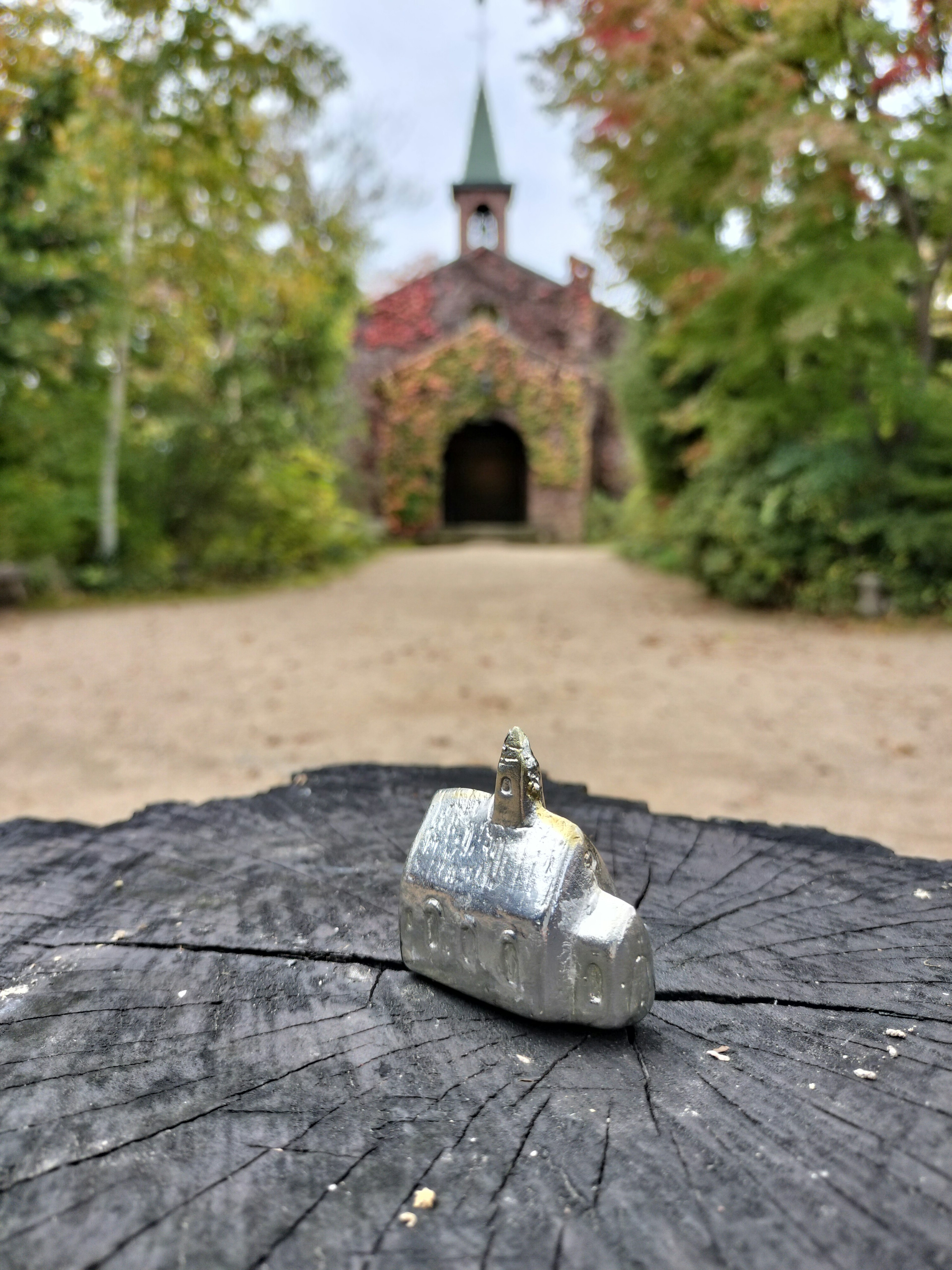 A small silver house model sits on a tree stump with a backdrop of autumn foliage and a church-like building