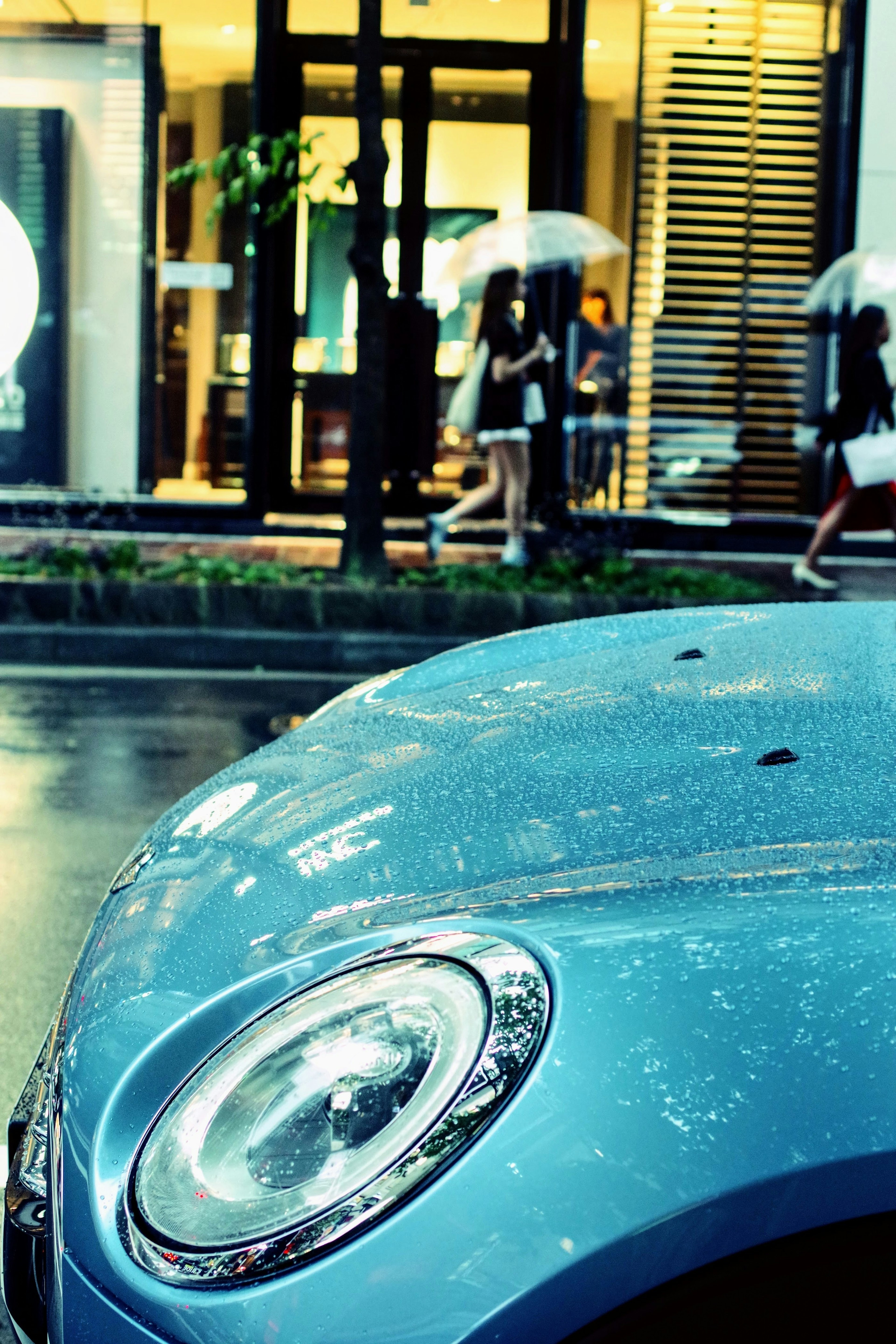 Blaues Auto mit Regentropfen und Fußgängern mit Regenschirmen