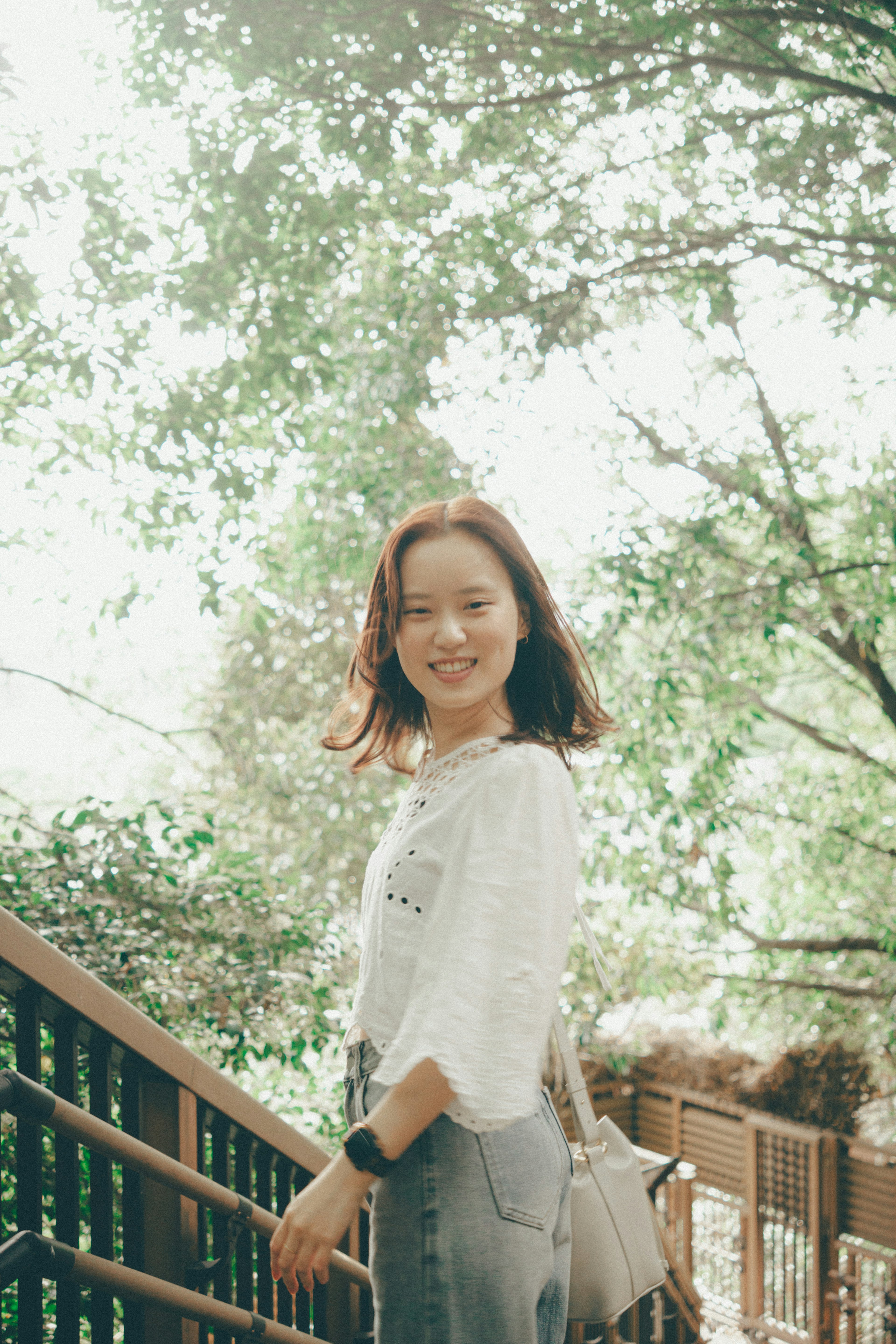 Une femme souriante parmi les arbres avec une lumière naturelle brillante