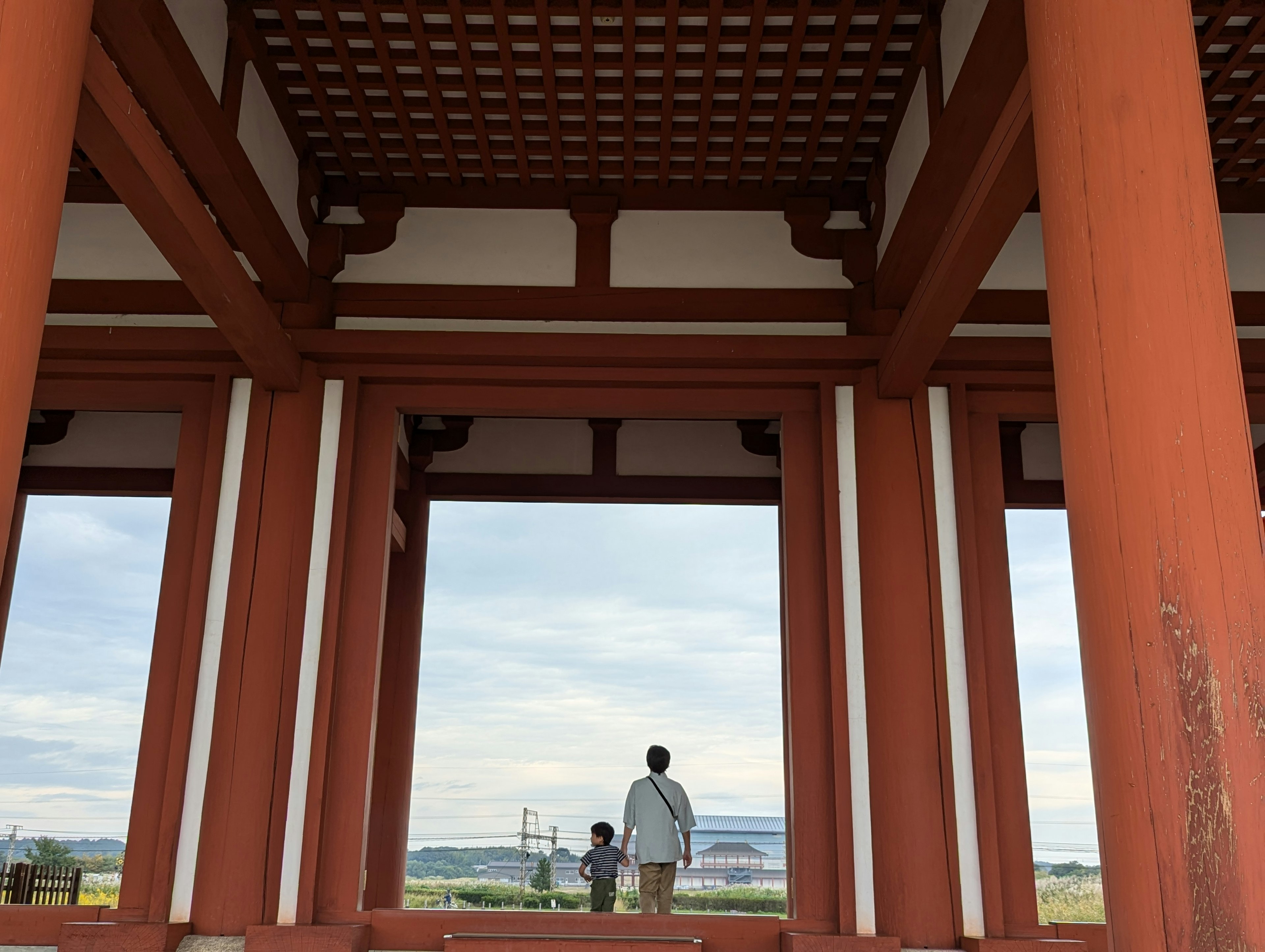 View of a traditional building with red pillars and a lattice ceiling featuring a parent and child