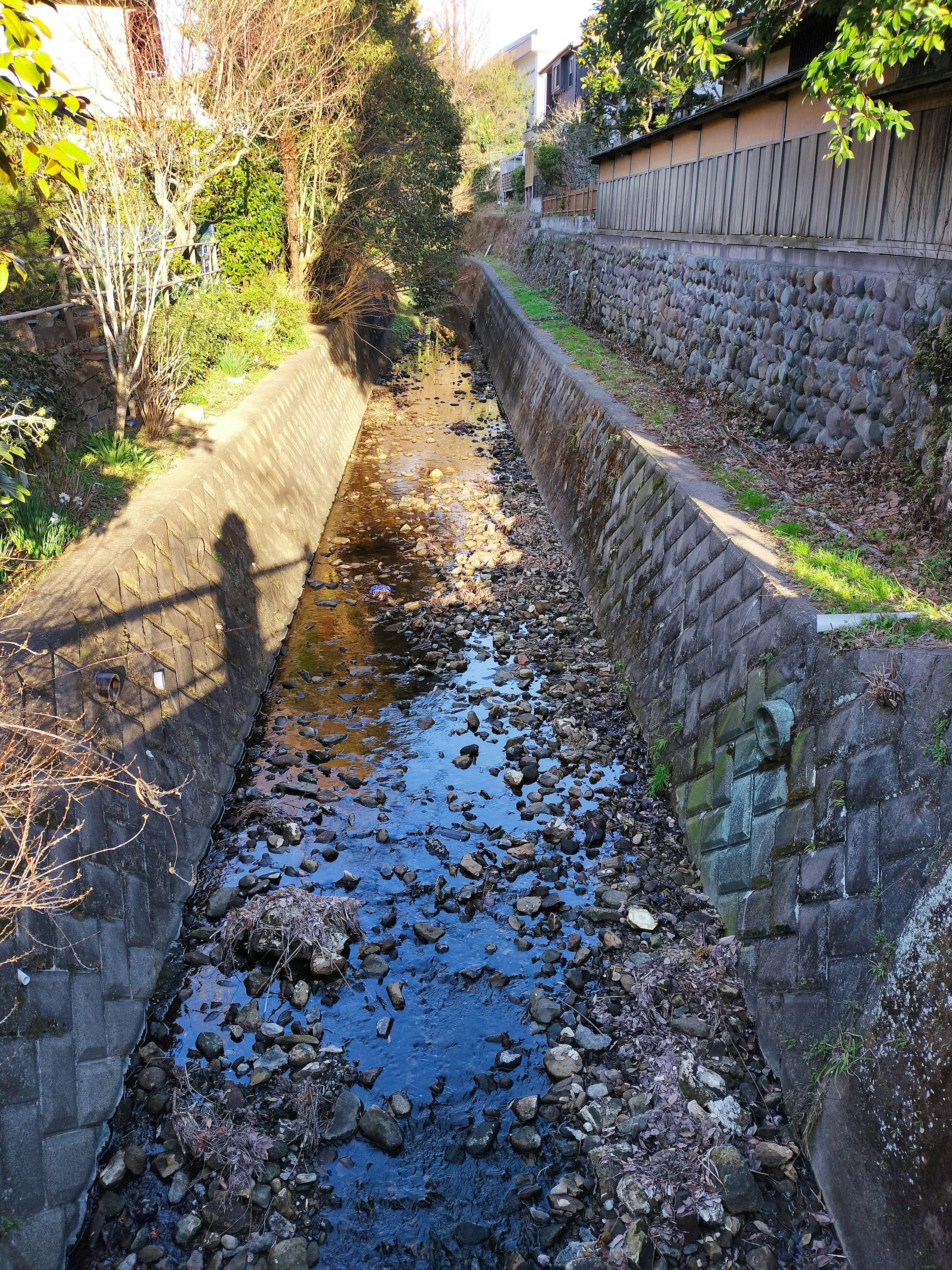 Schmaler Bach mit niedrigem Wasserstand umgeben von Steinmauern und Grünflächen