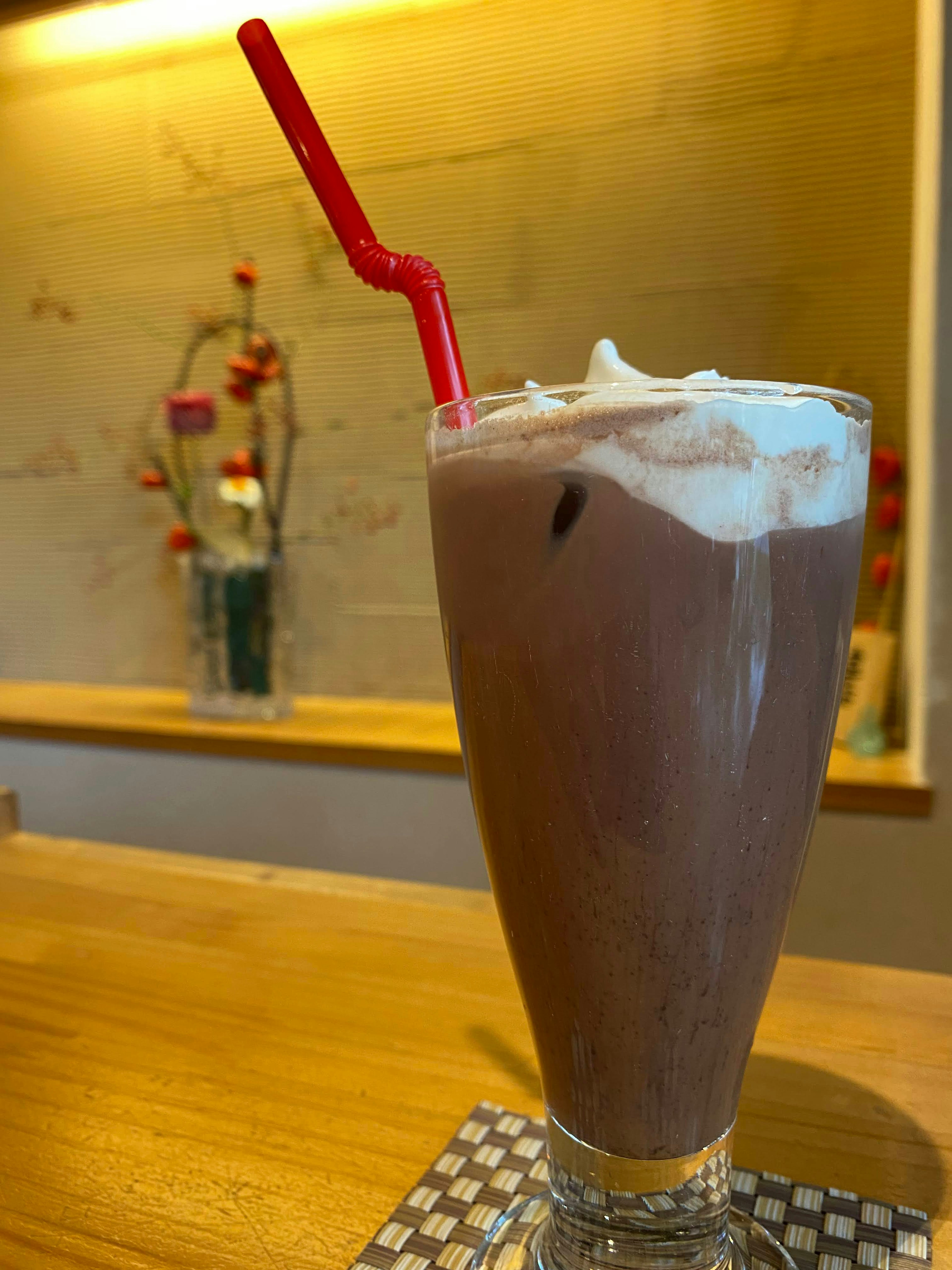 Une boisson au chocolat surmontée de crème dans un verre avec une paille rouge