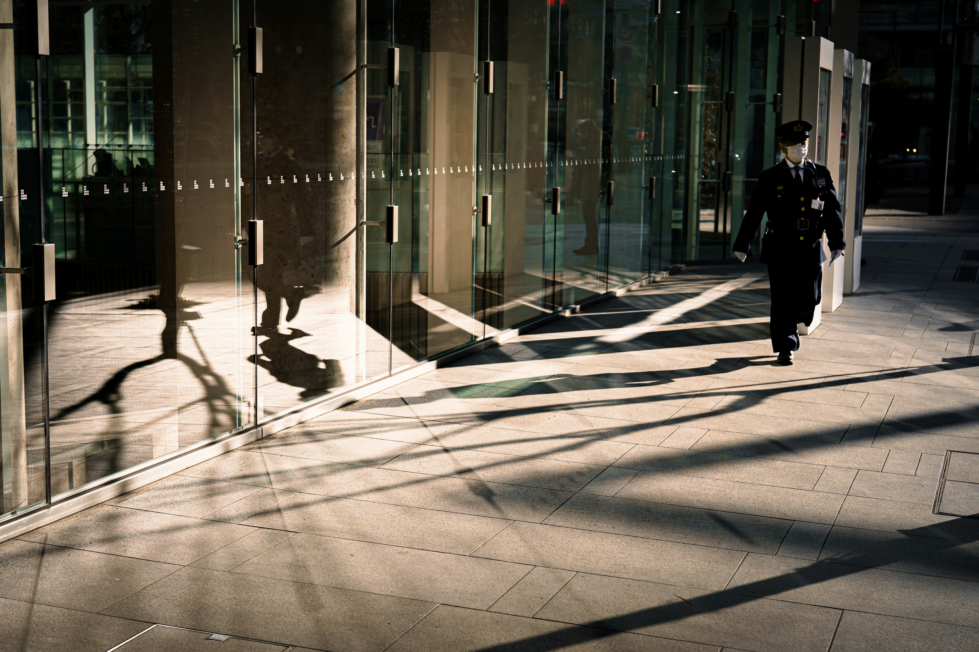 A police officer walking past a glass building with shadows