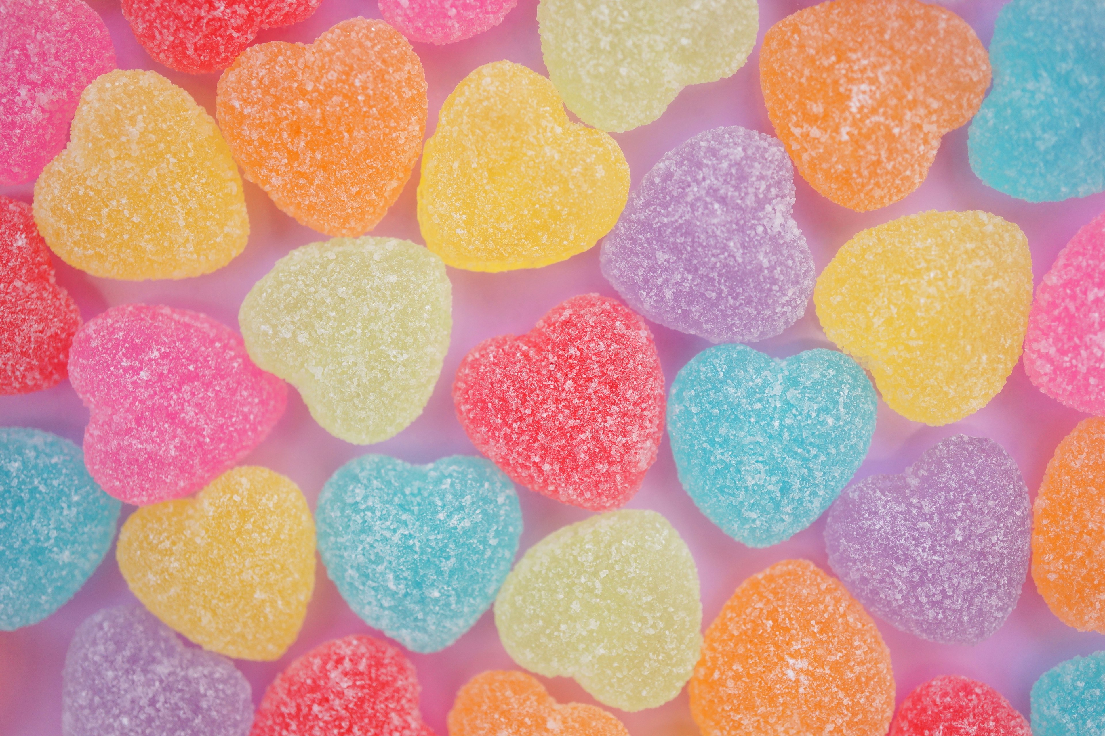 Dulces de goma en forma de corazón de colores esparcidos sobre un fondo rosa