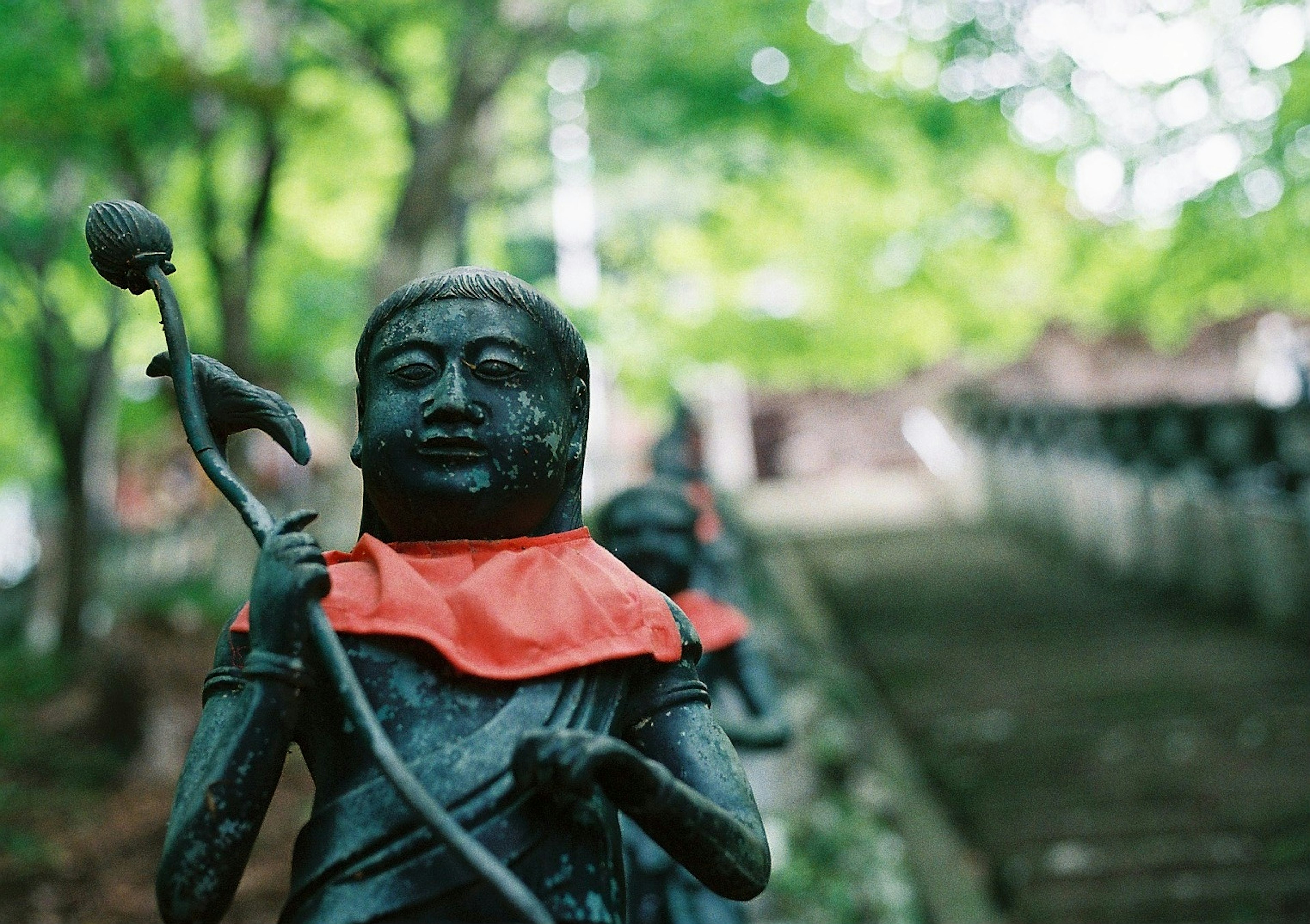 赤い布を着た彫刻の像が並ぶ緑豊かな風景