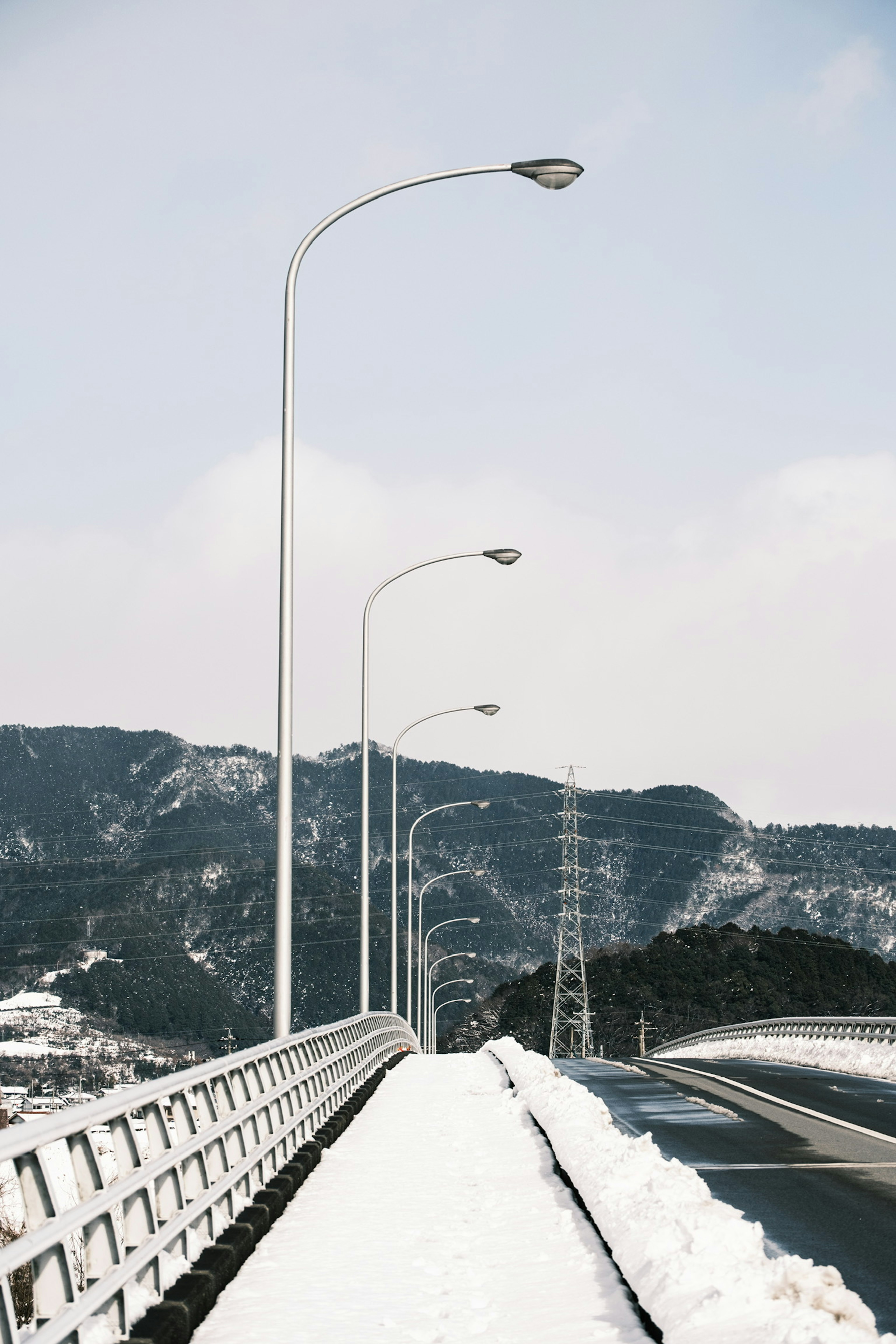 Row of streetlights on a snow-covered bridge with mountains in the background