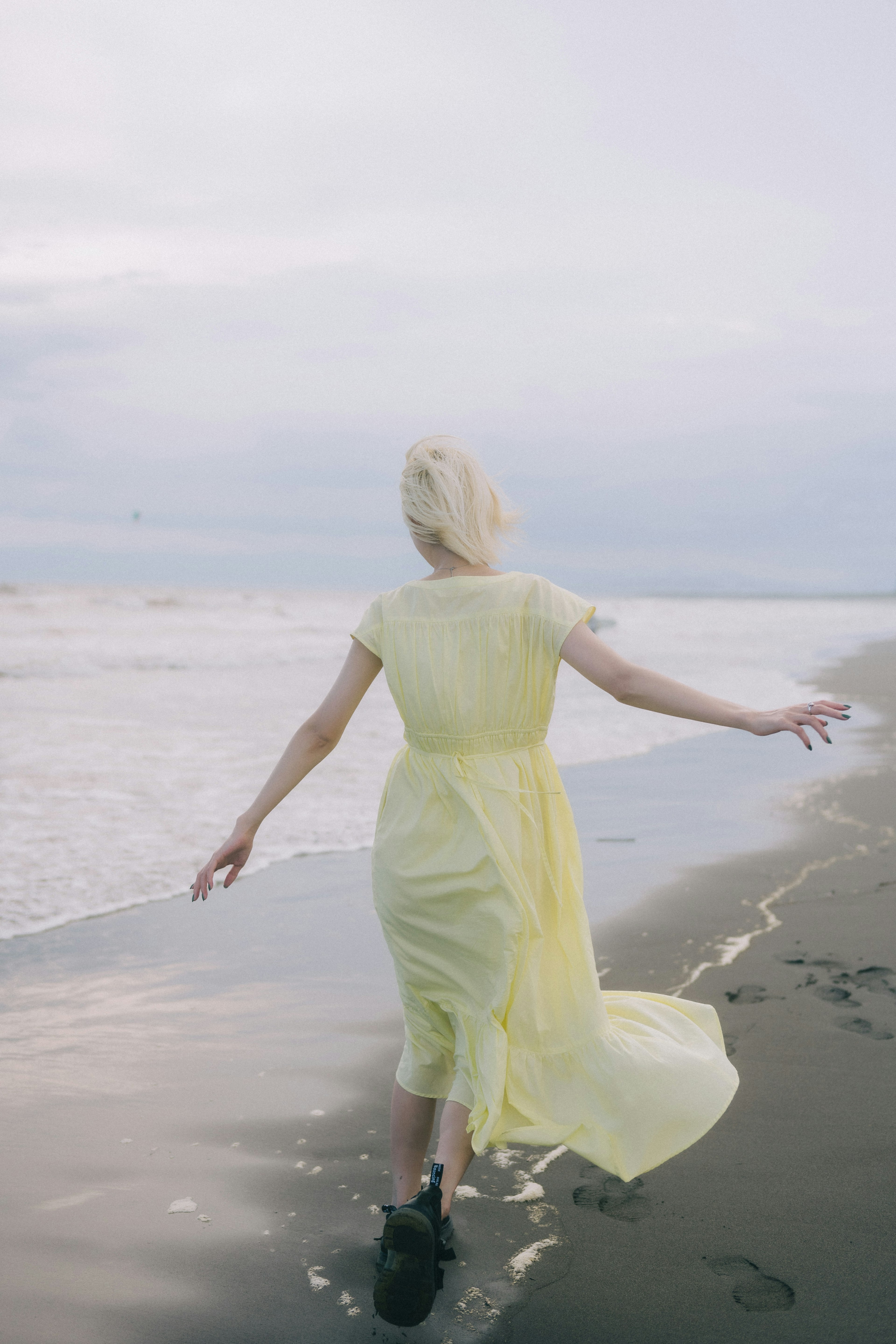 Una mujer con un vestido amarillo caminando por la playa de espaldas