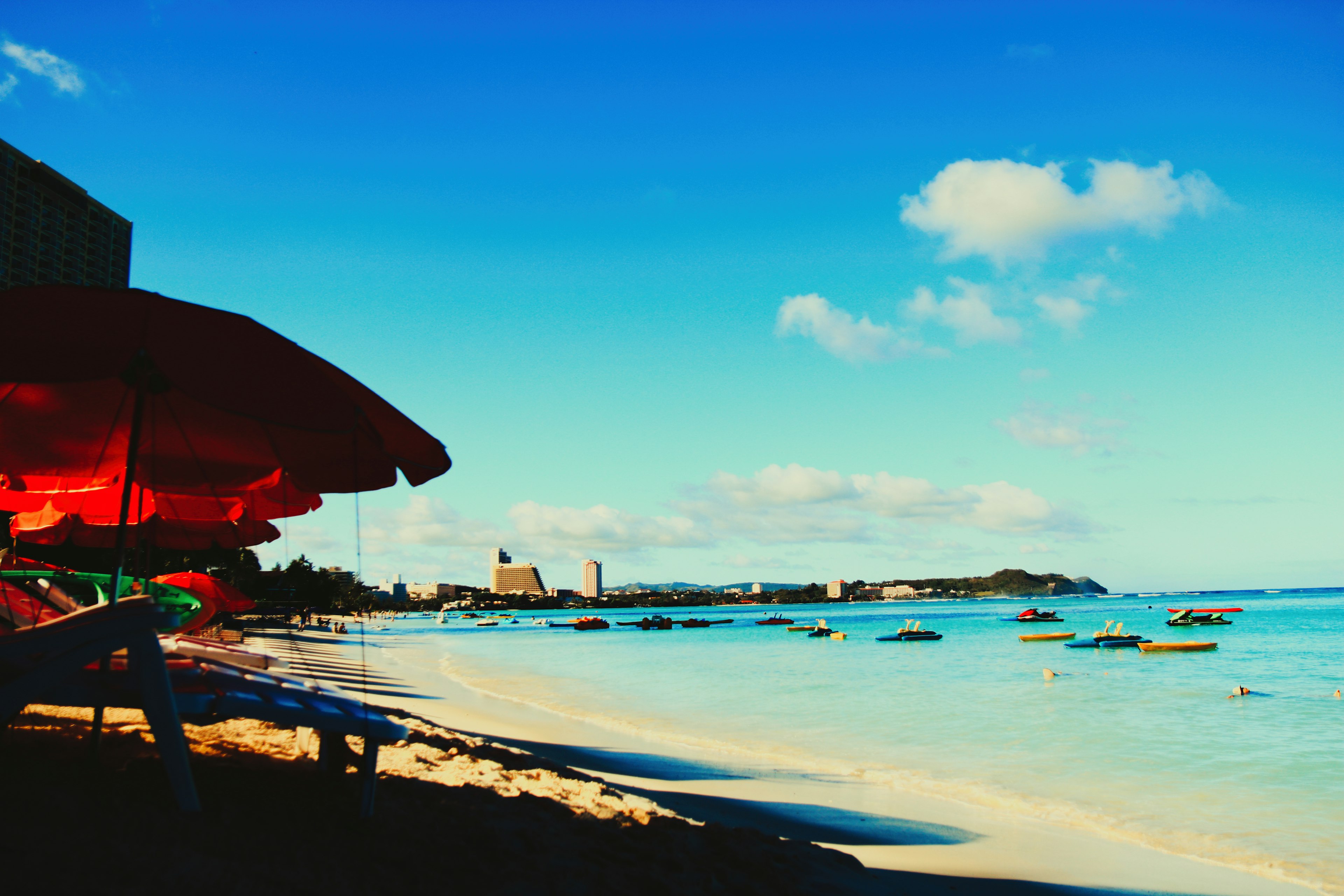 Escena de playa con sombrillas rojas y agua turquesa bajo un cielo azul