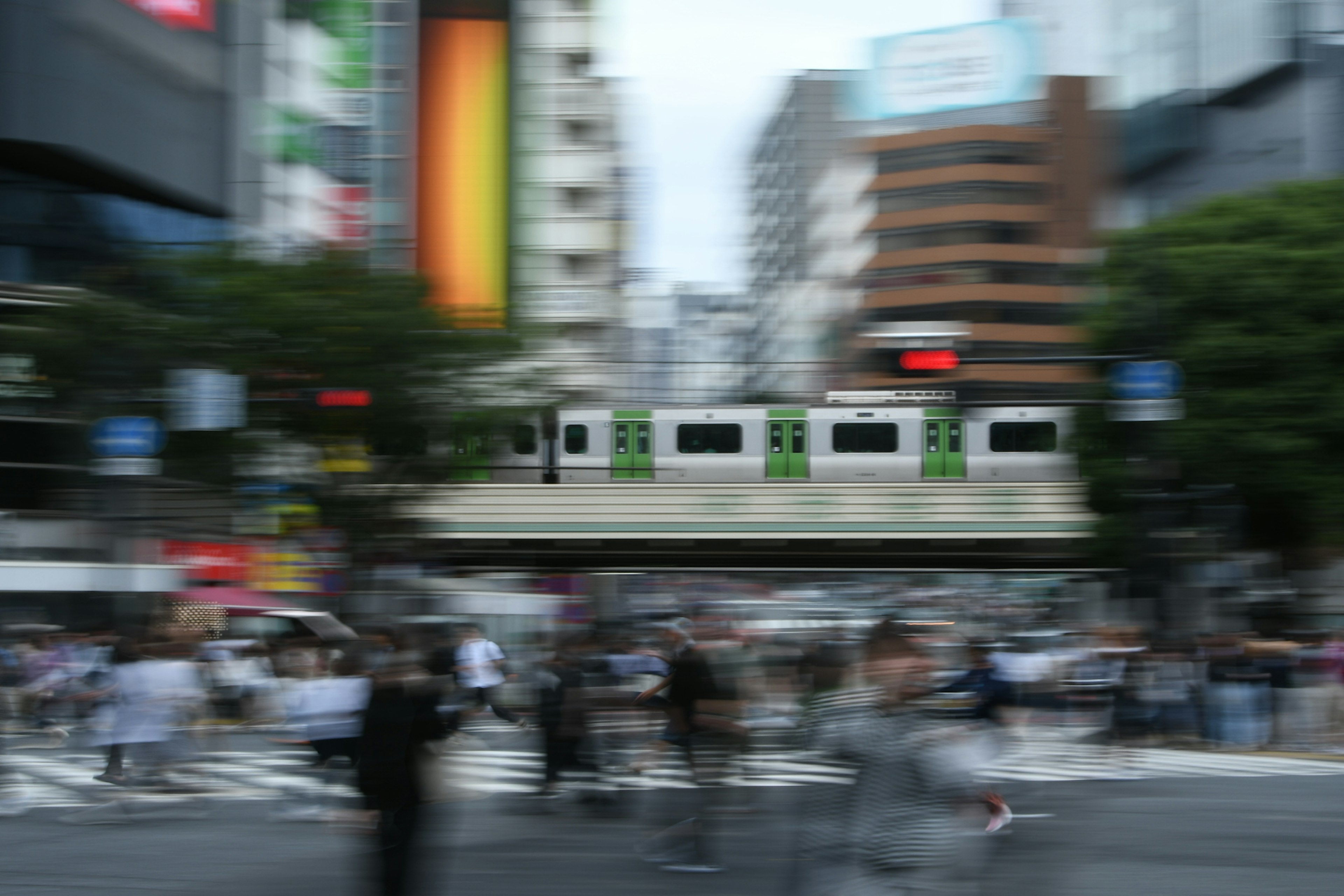 Grüner Zug, der durch eine belebte Kreuzung in Tokio mit Menschenmengen fährt