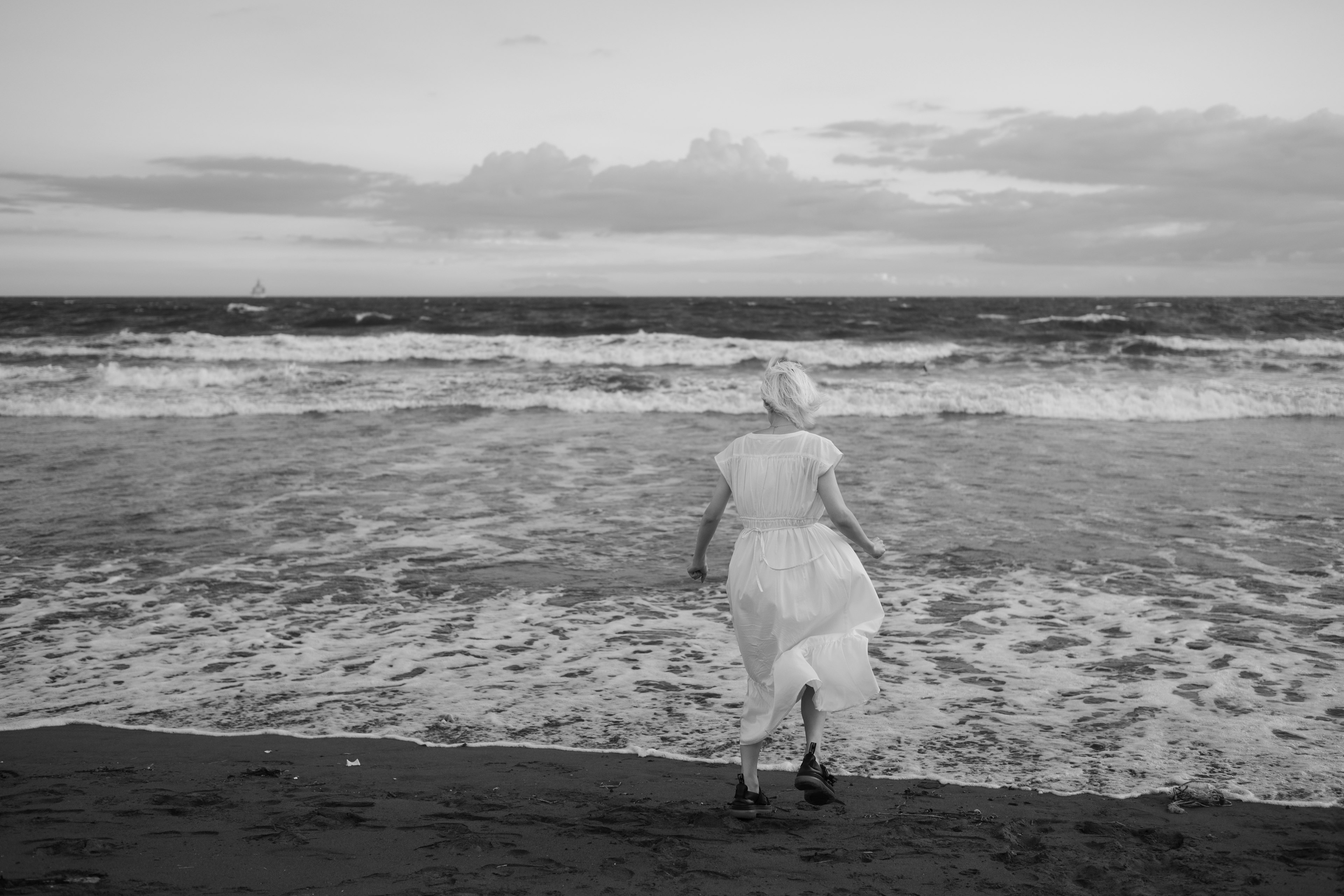 A woman in a white dress standing at the shoreline in black and white