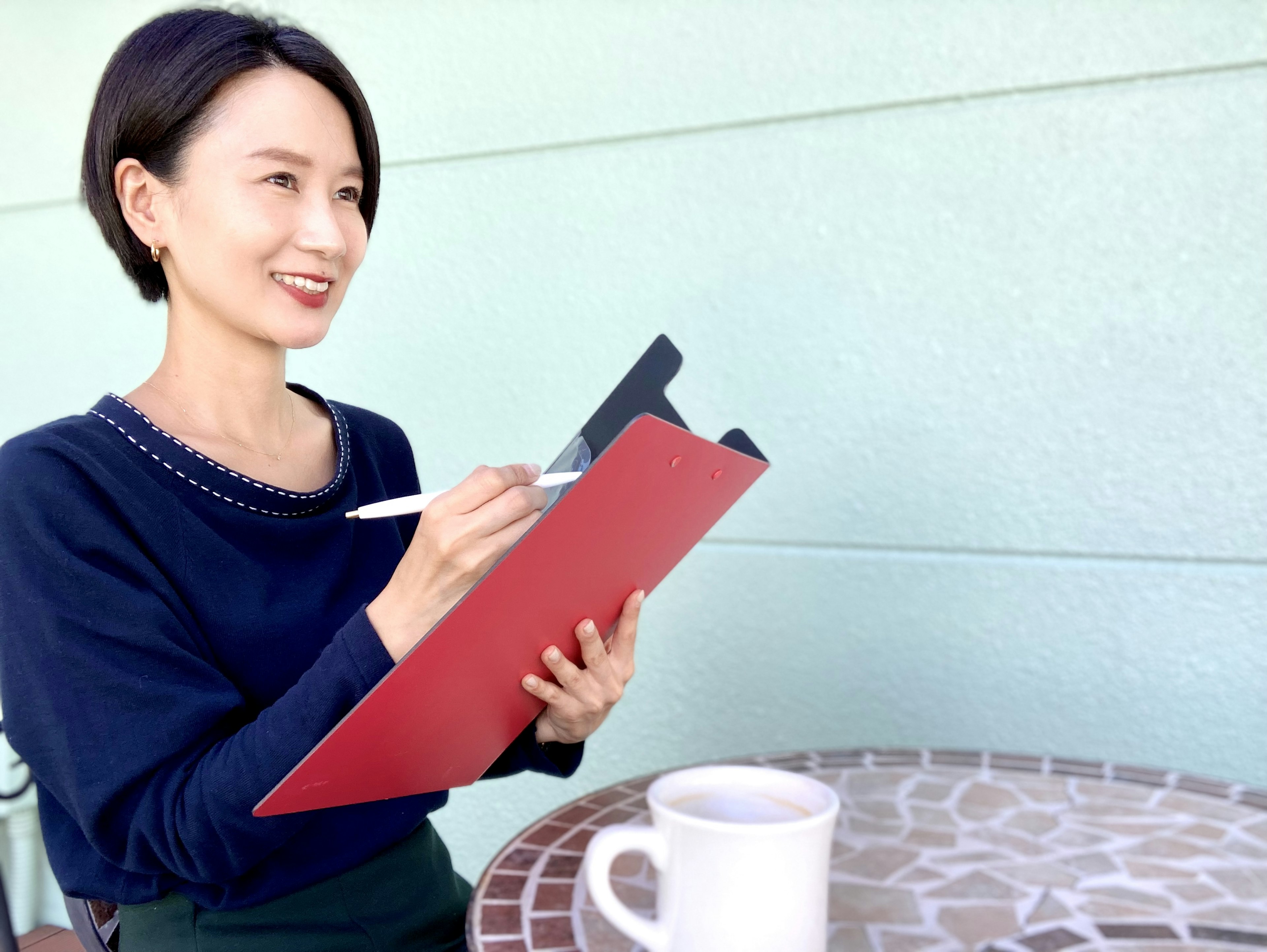 Una donna che sorride mentre tiene un clipboard rosso e scrive con una penna