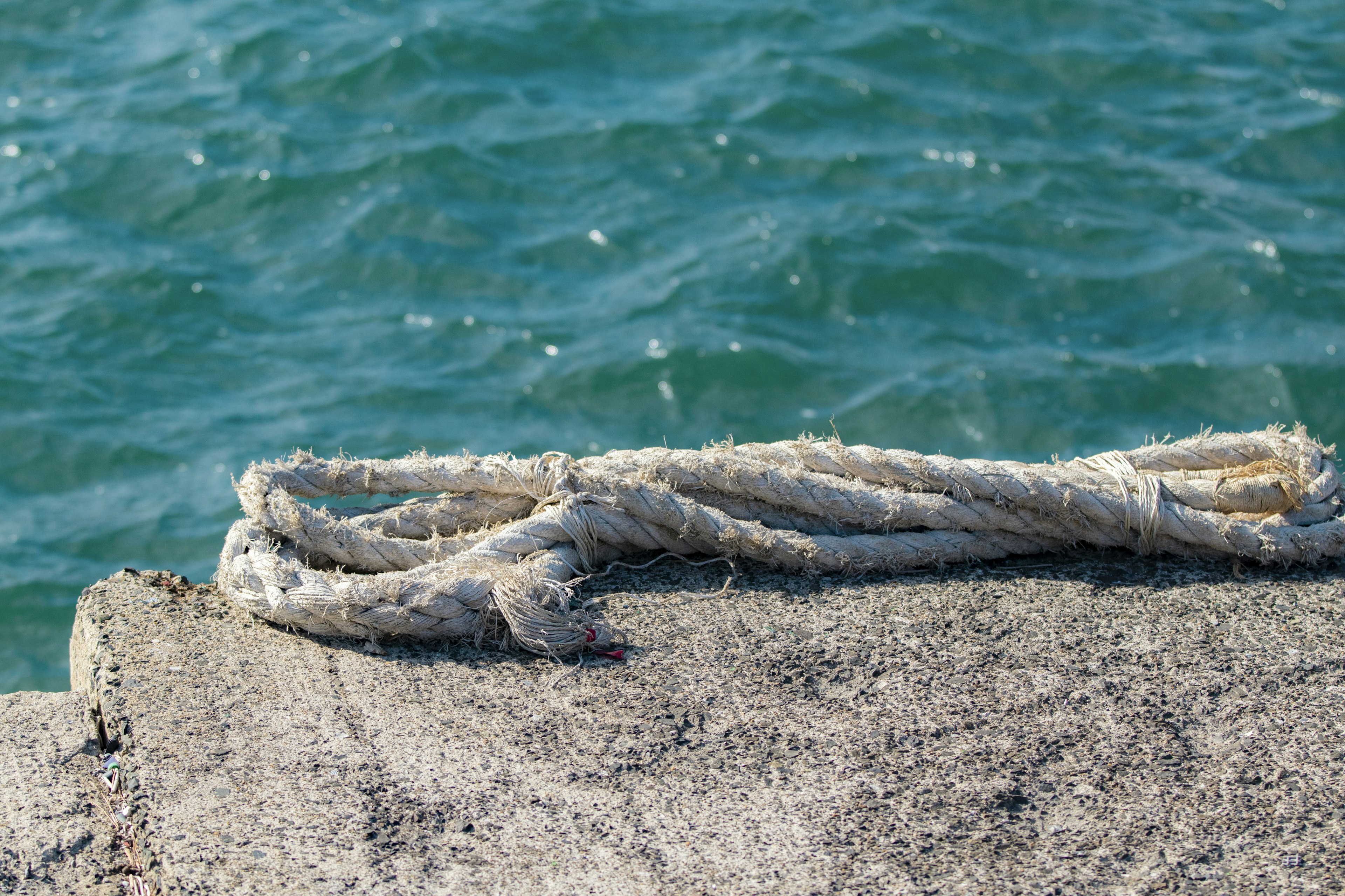 Close-up of an old rope resting on a stone surface near water