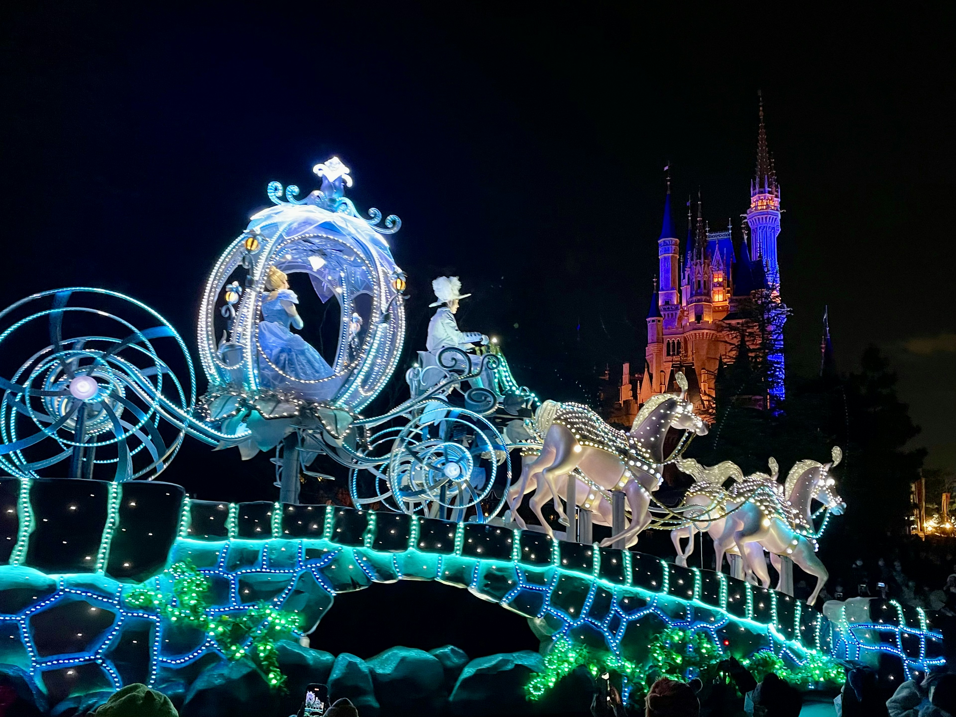 Cinderella's illuminated carriage during a nighttime Disney parade with a castle backdrop