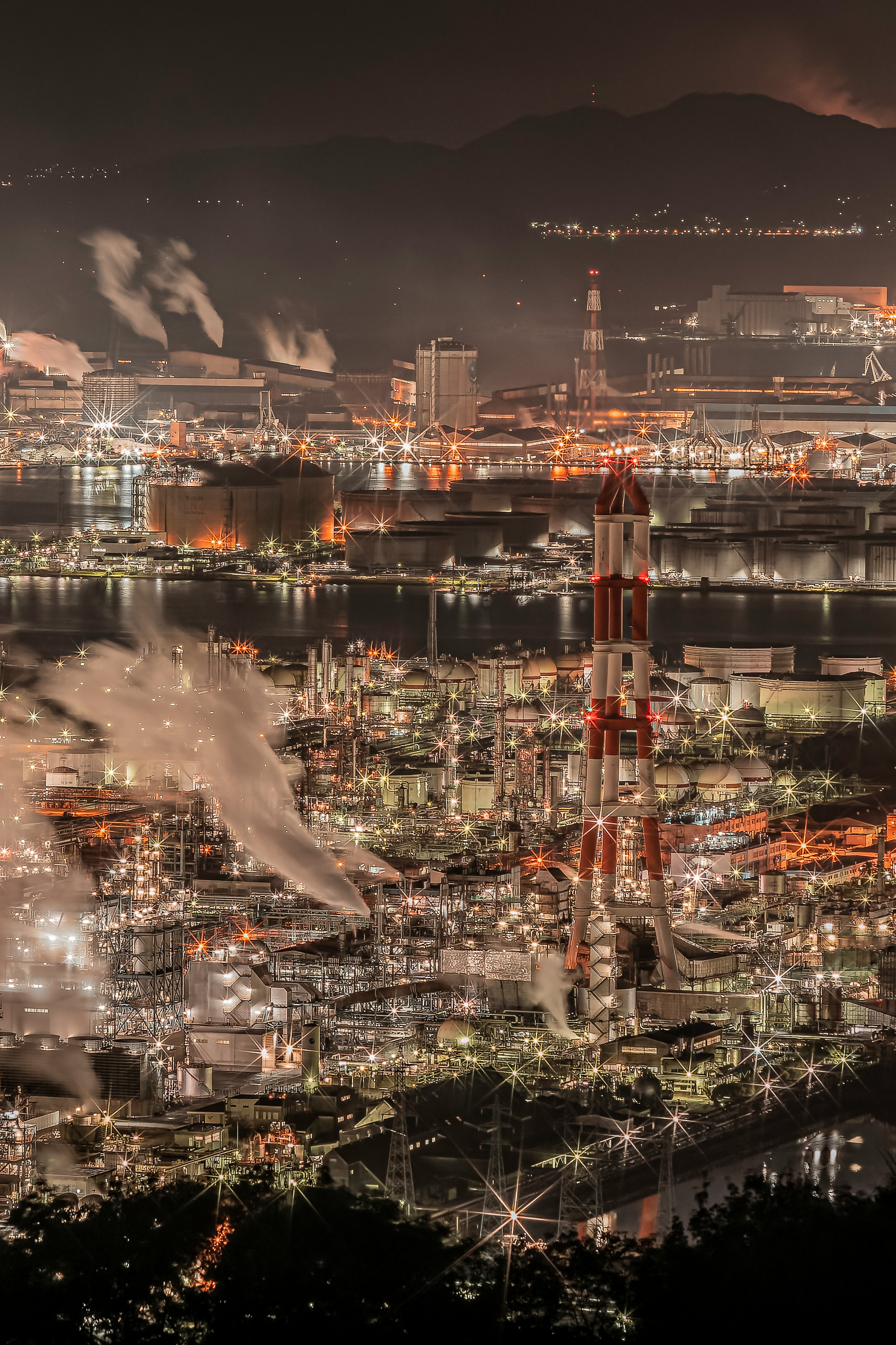 夜景の工業地帯の全景明るい光と煙の煙突