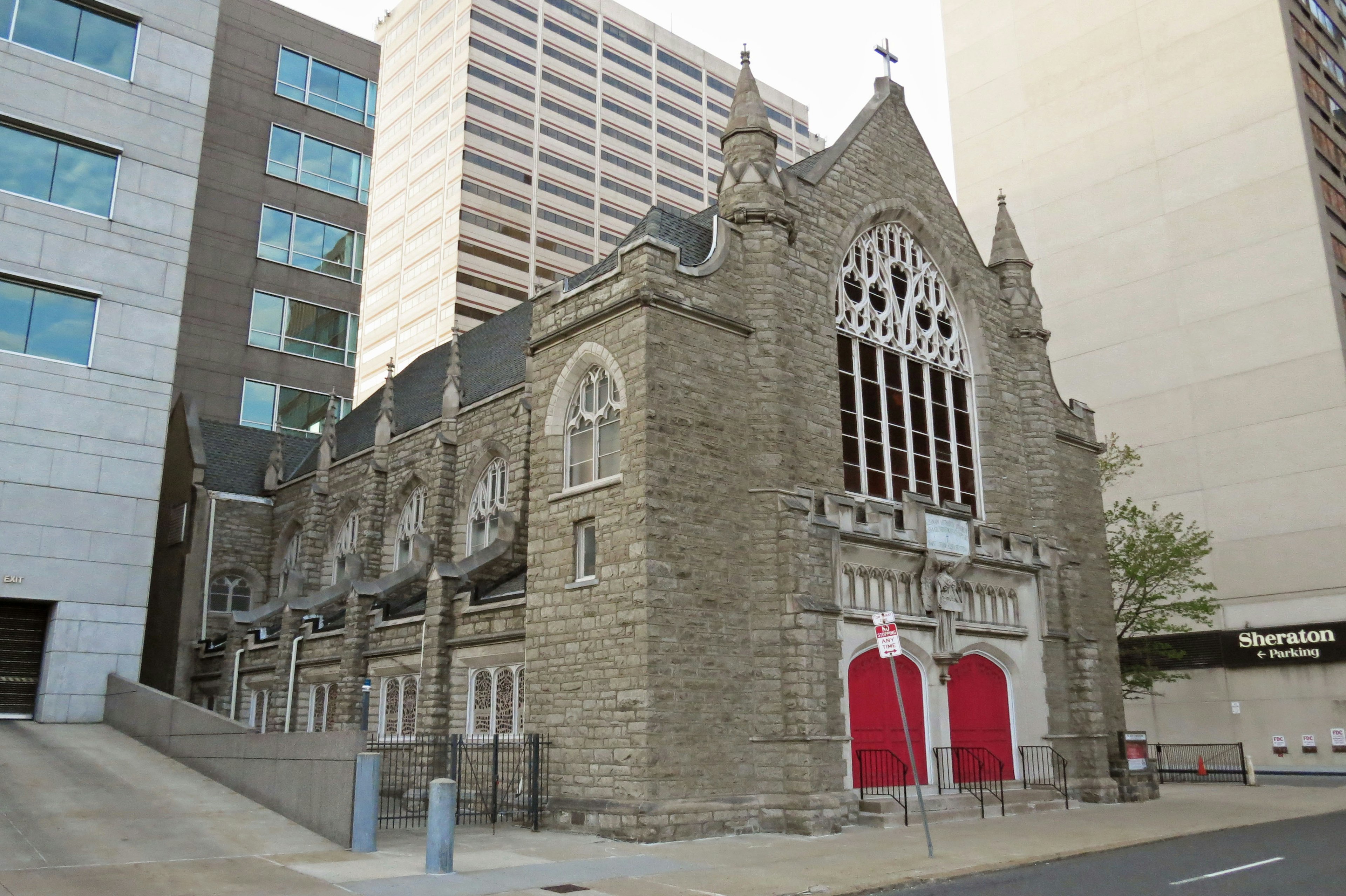 Historic stone church with red doors contrasting with modern buildings