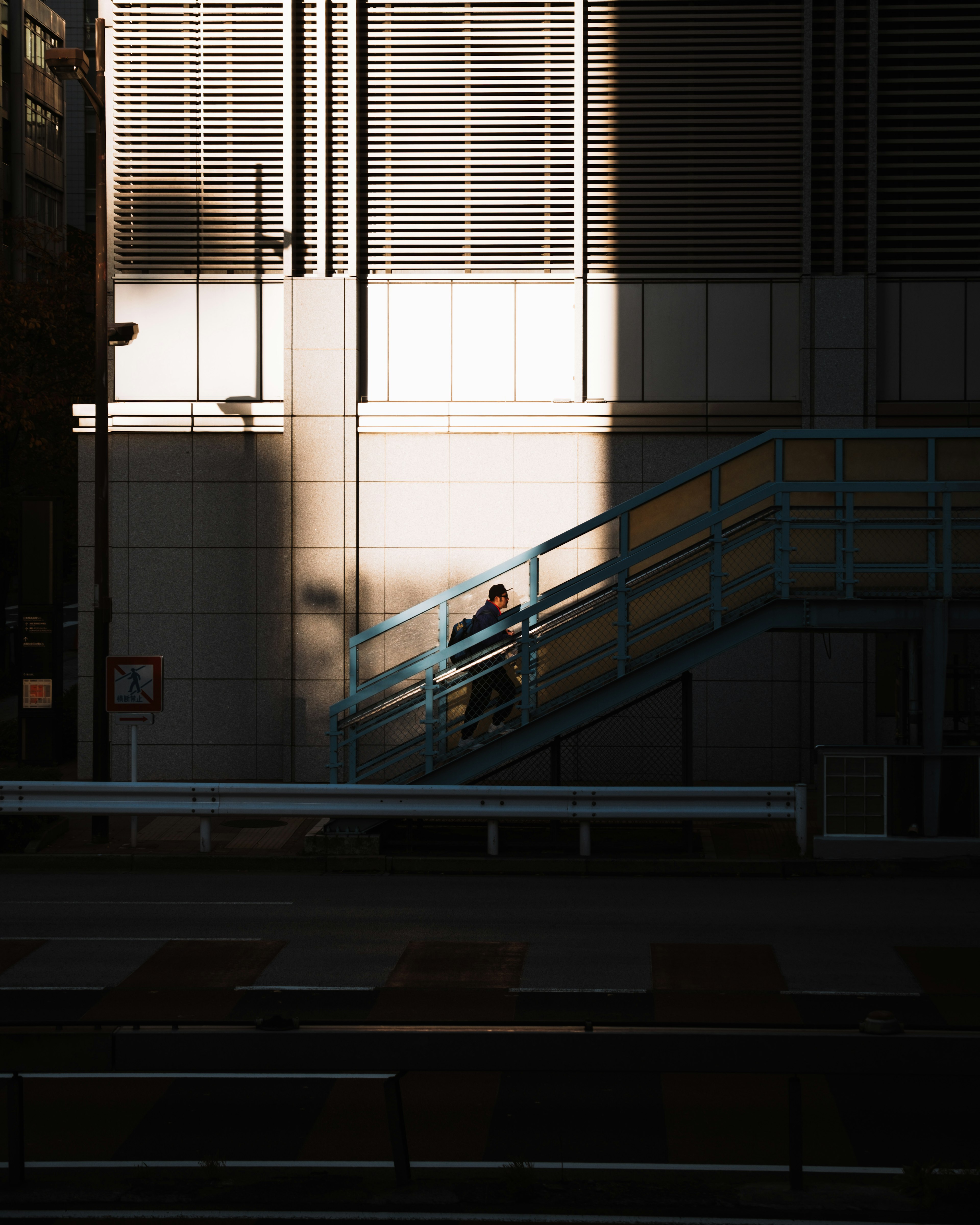 Silhouette d'une personne montant un escalier bleu contre la façade d'un bâtiment