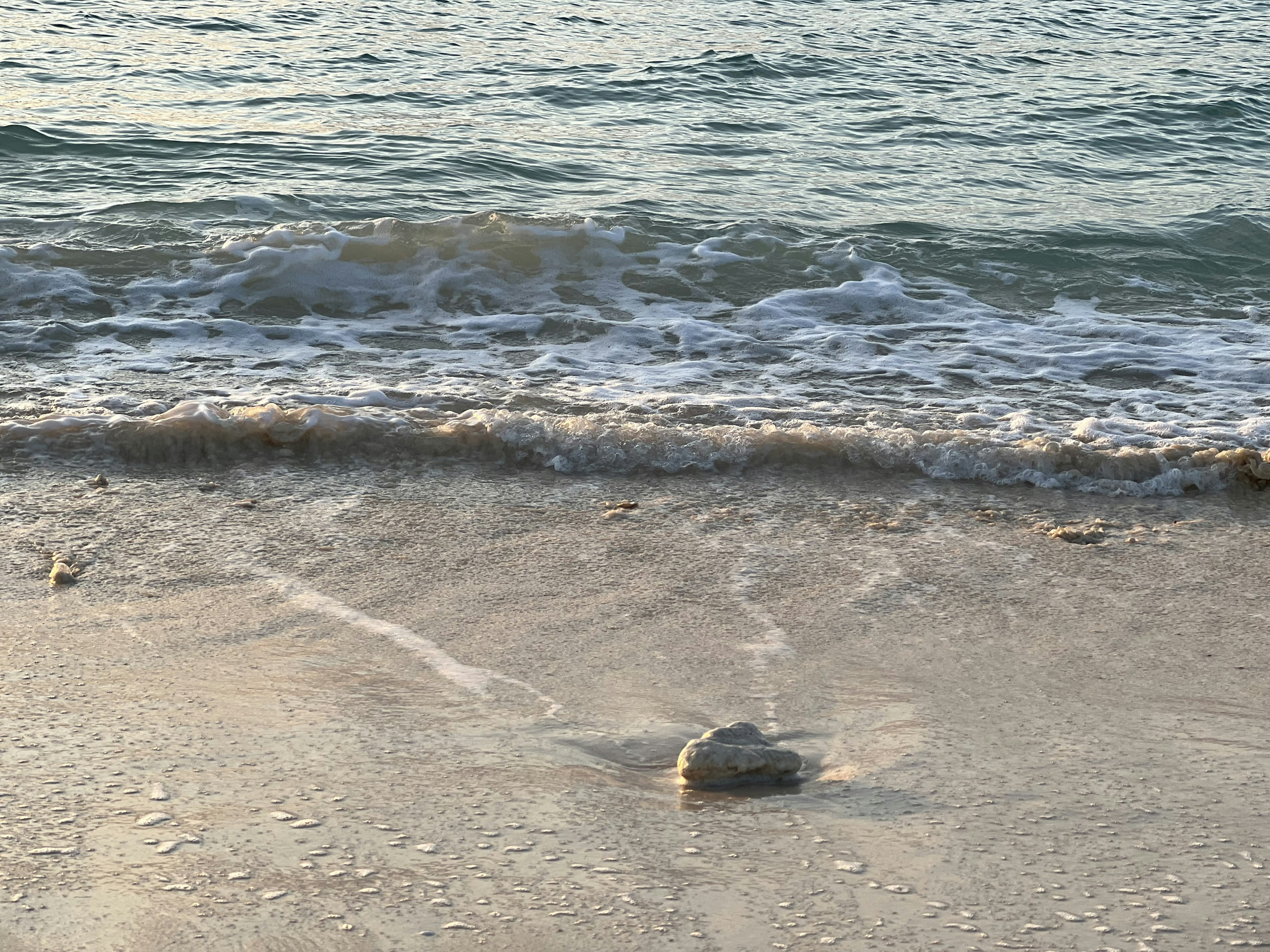 Roccia su una spiaggia di sabbia con onde leggere