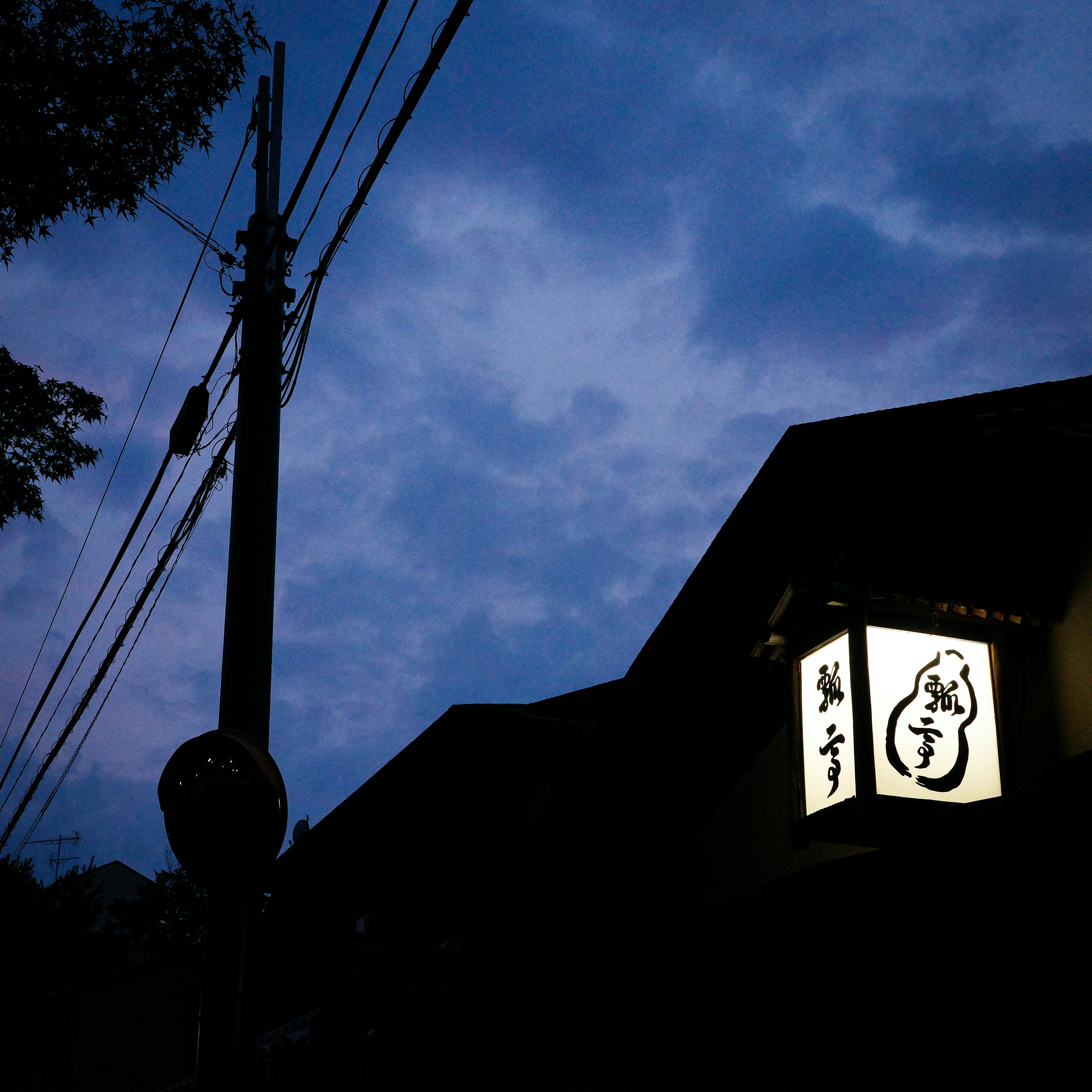 Cartel de restaurante japonés iluminado al anochecer bajo un cielo nublado