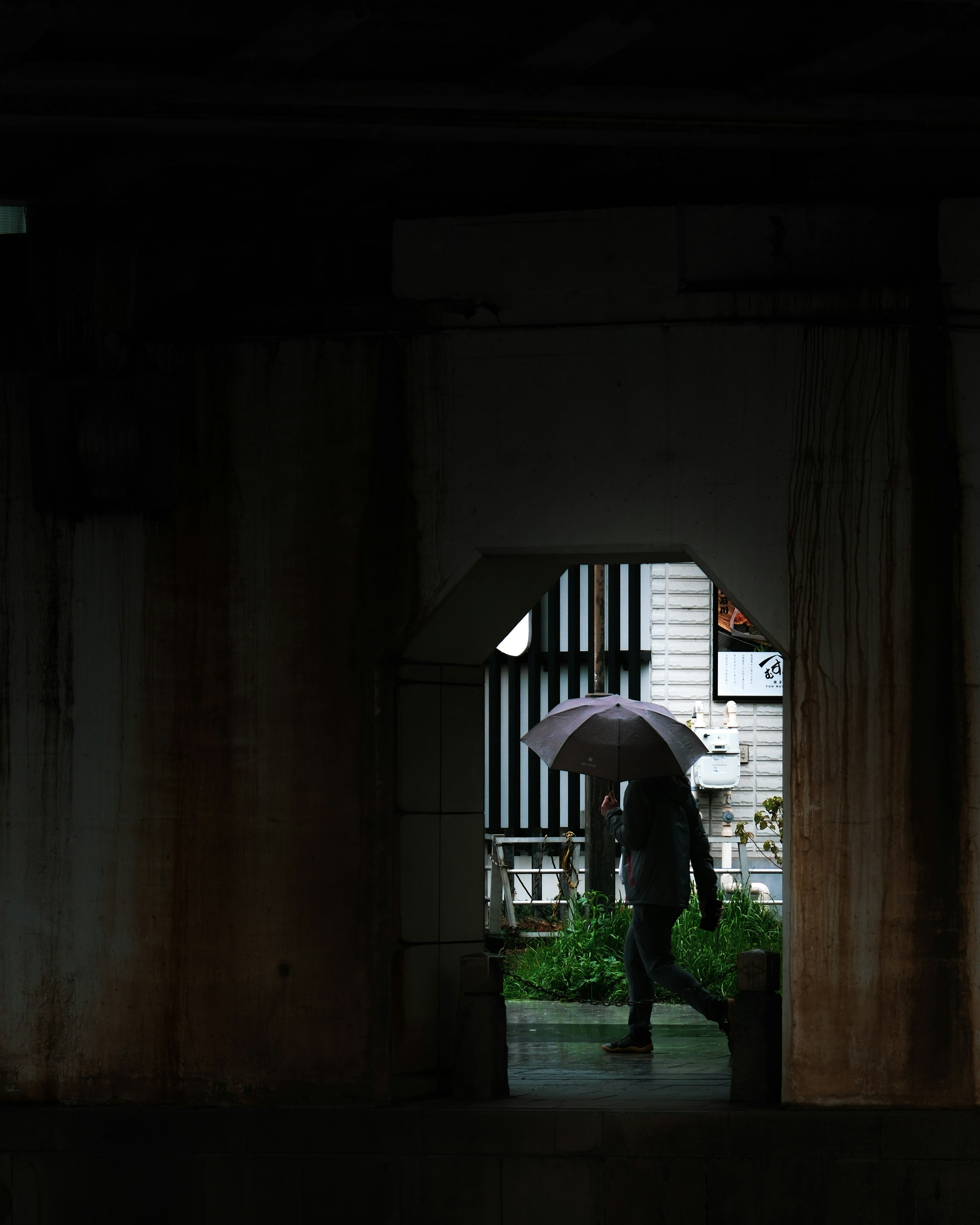 Una silhouette di una persona che cammina con un ombrello attraverso un arco sotto la pioggia