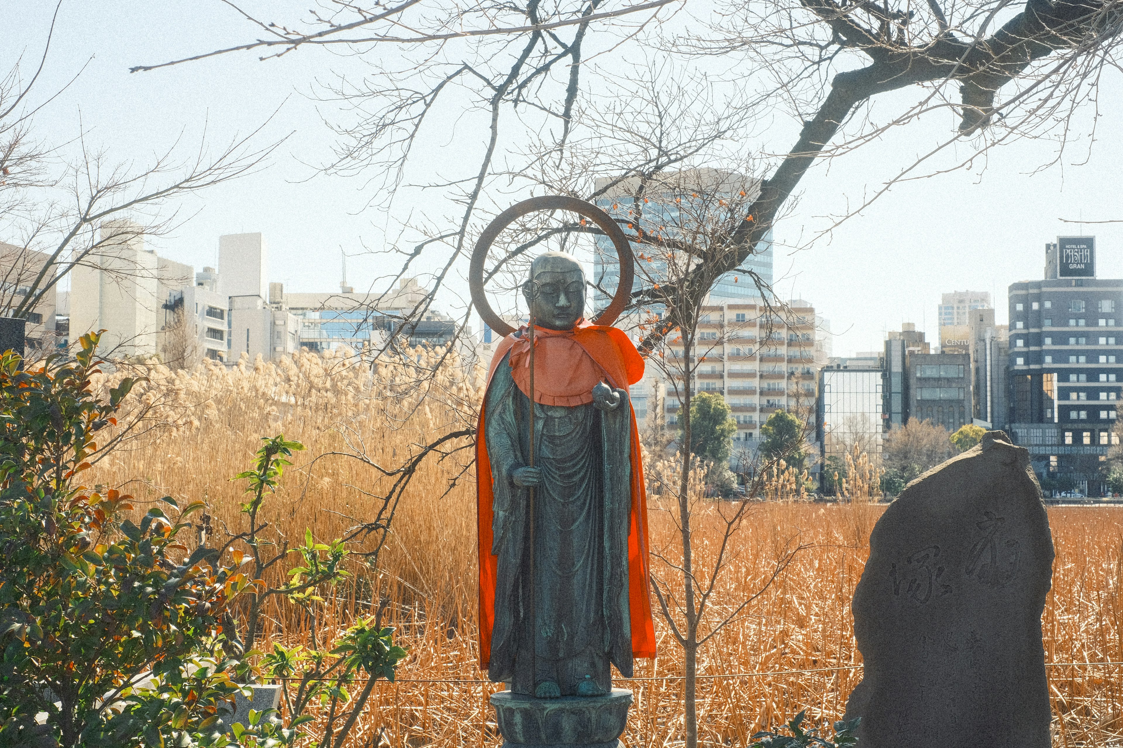 A statue wearing a red cape stands against a city backdrop