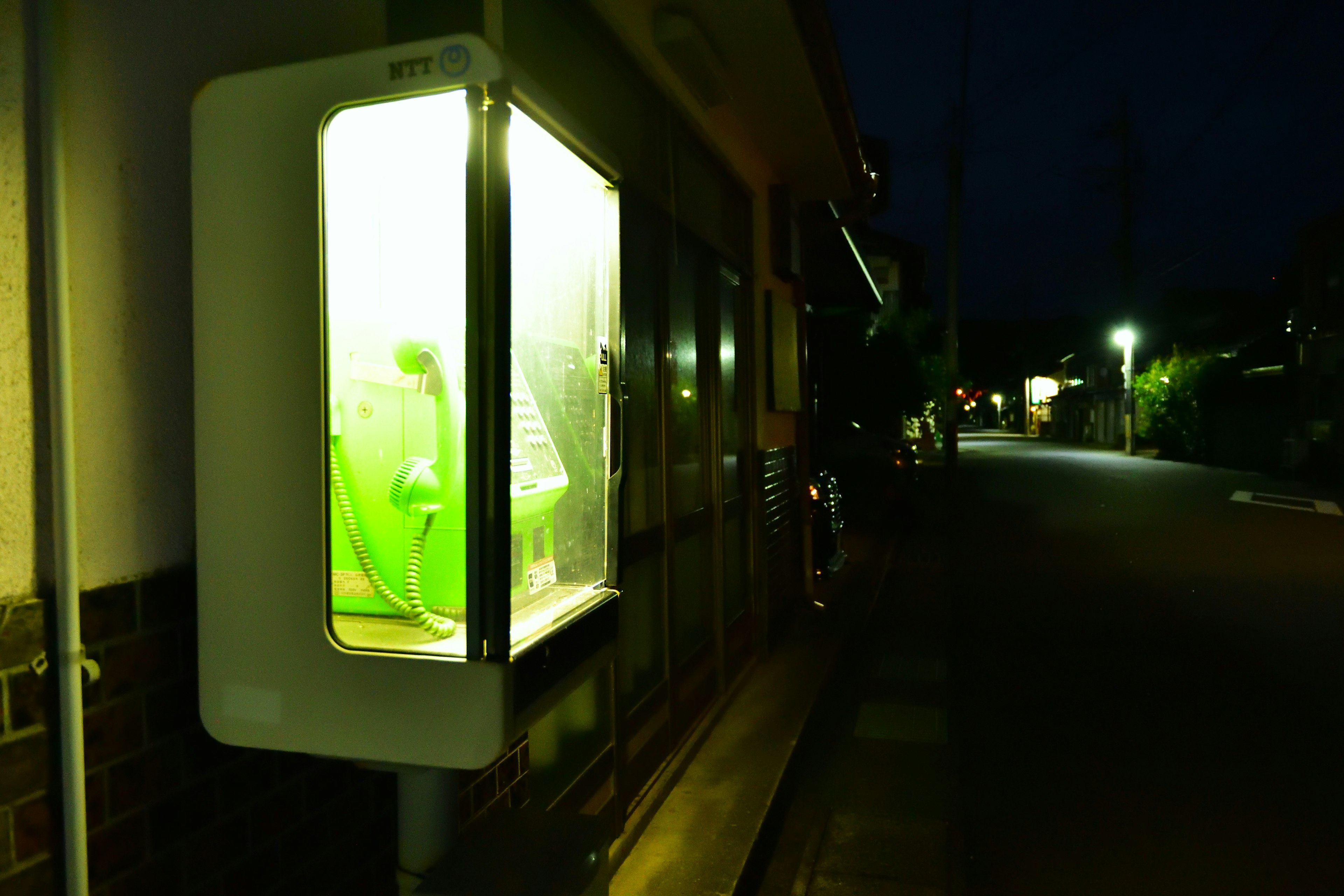 A glowing green telephone booth on a street at night