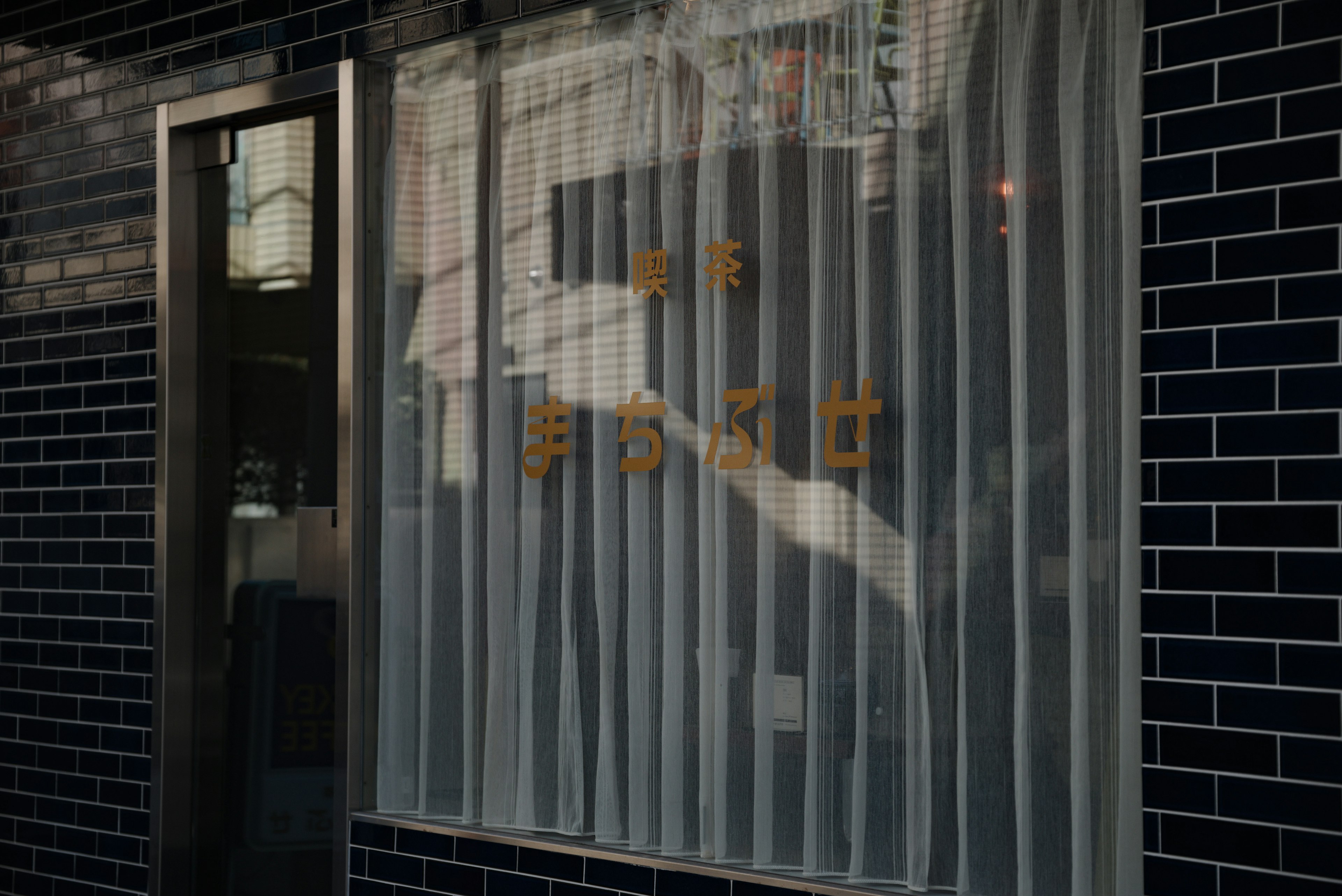 Ein Fenster mit weißen Vorhängen und goldenem Text an einer schwarzen Fliesenwand