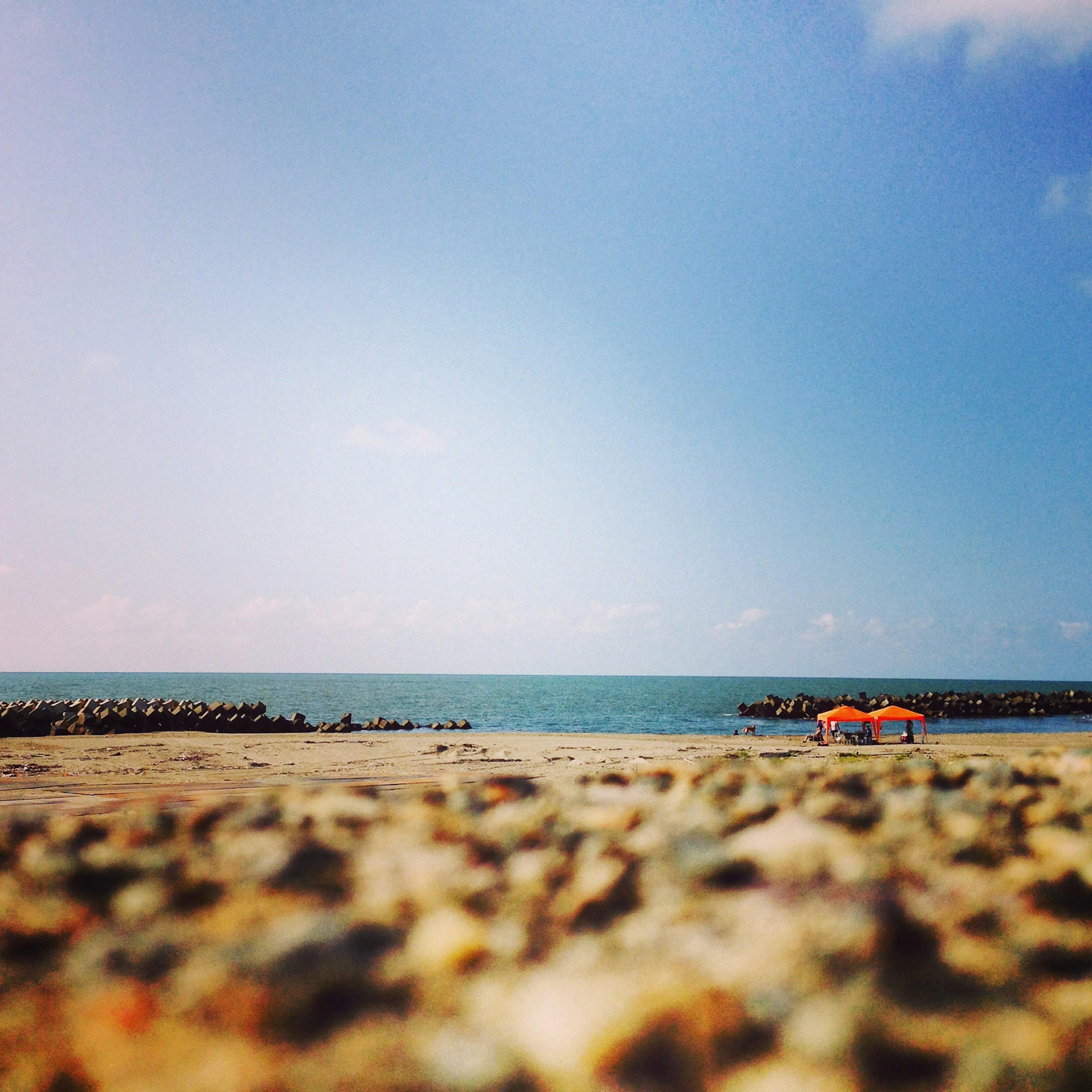 A scenic view of blue sea and sky with sandy beach and a small red-roofed hut