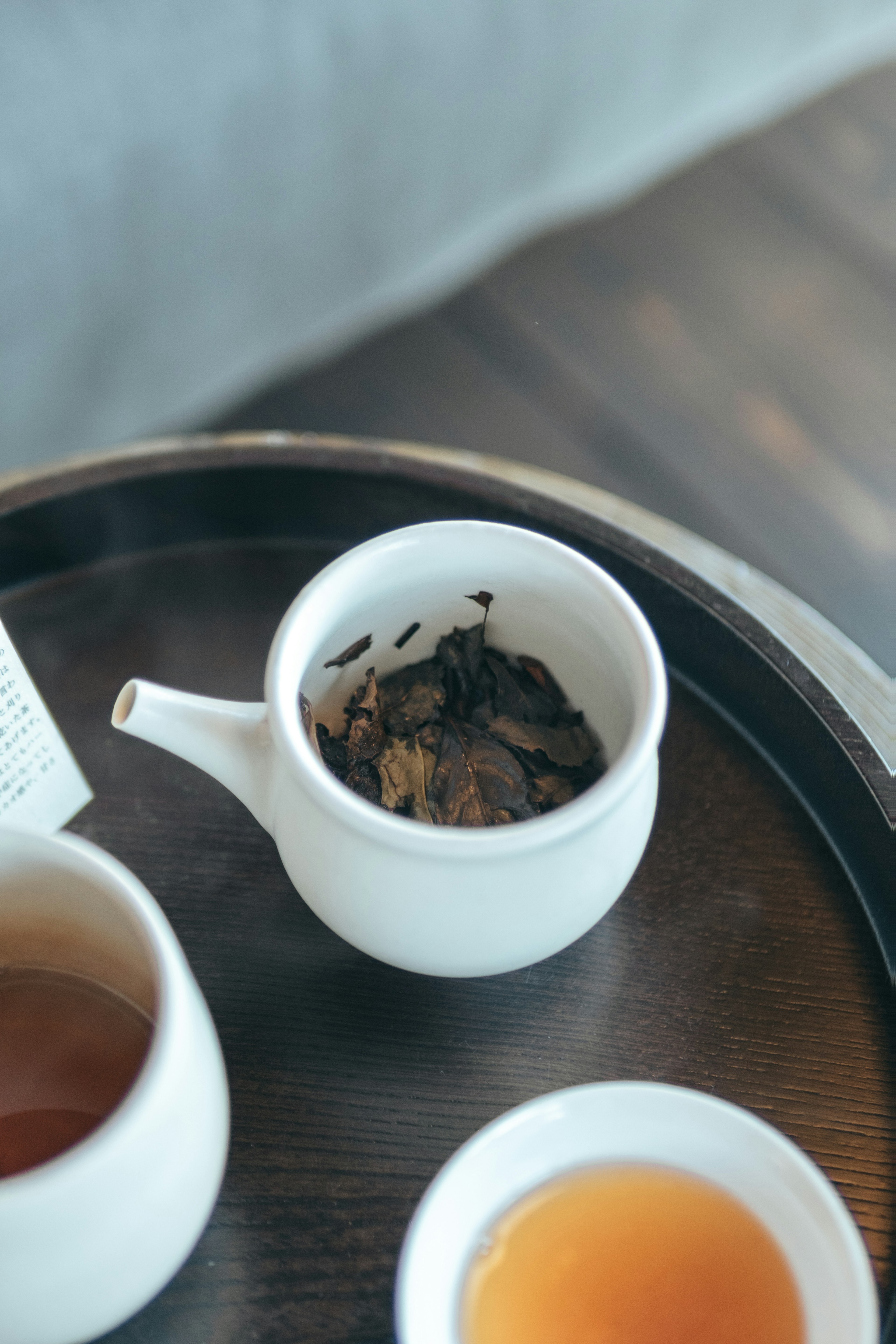 Théière blanche avec des feuilles de thé et des tasses sur un plateau en bois