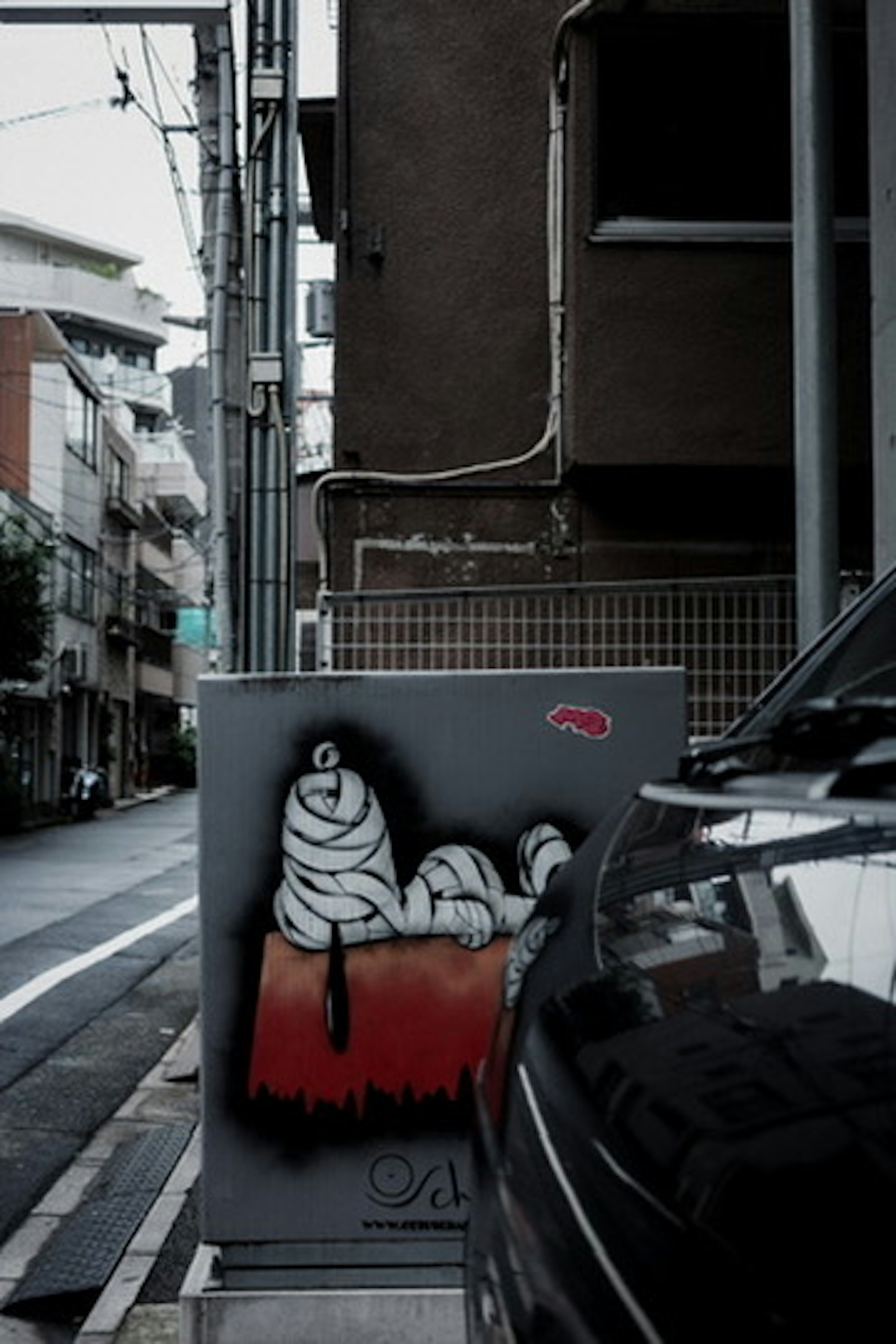 Esquina urbana con arte de graffiti en una caja eléctrica y un coche negro