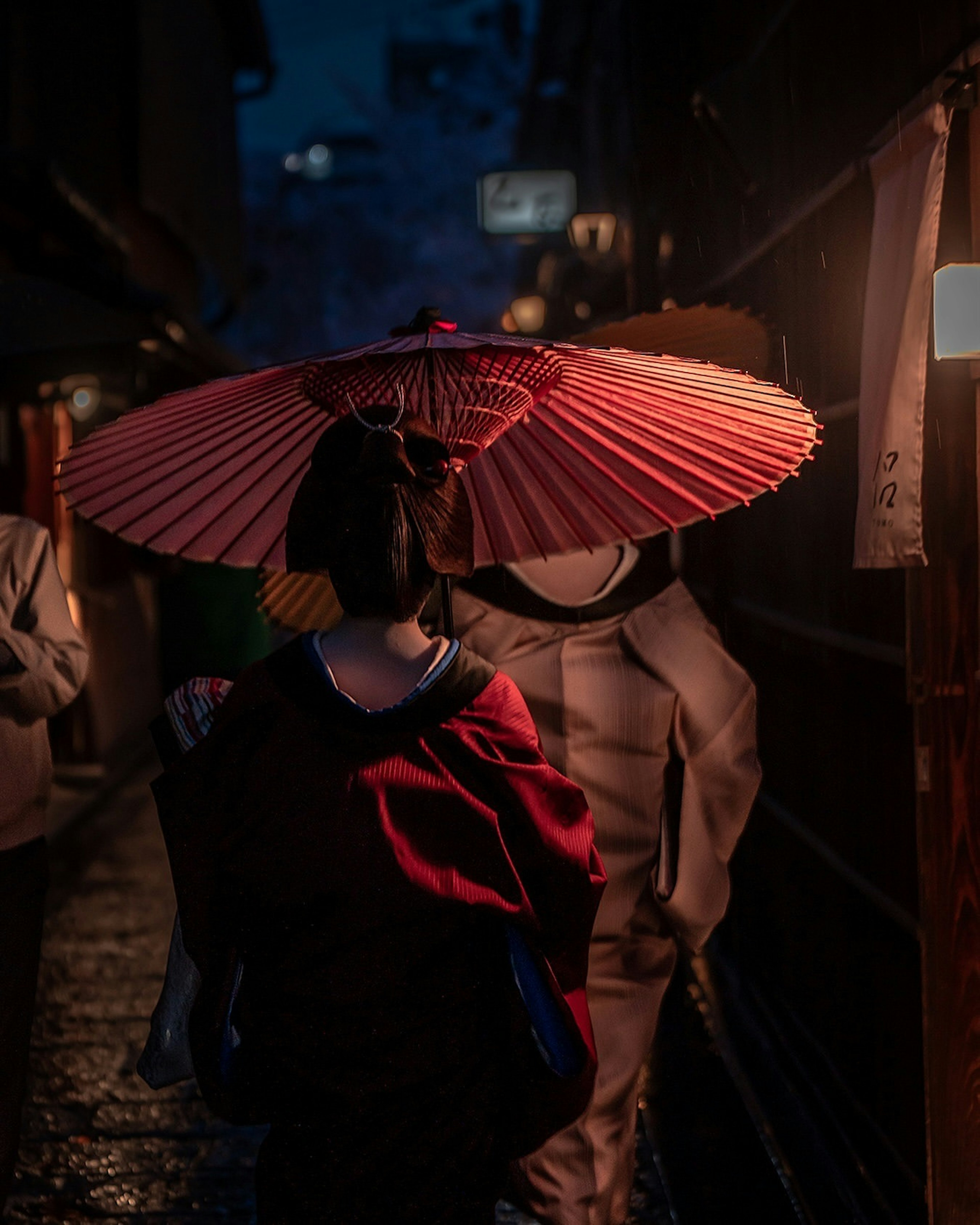 夜の街を歩く女性が赤い傘を持っている