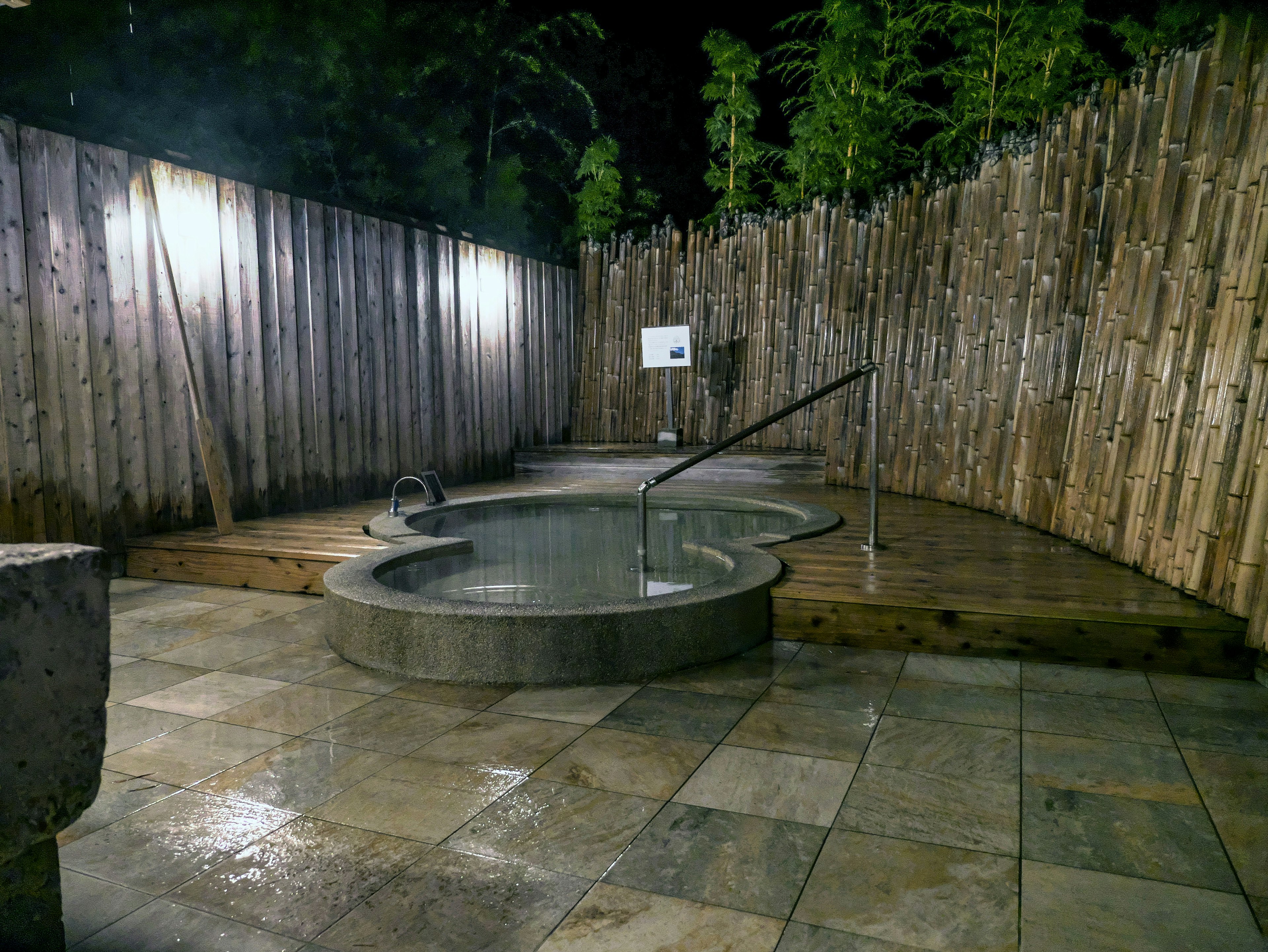 Escena de jacuzzi al aire libre por la noche con cerca de madera y baldosas de piedra