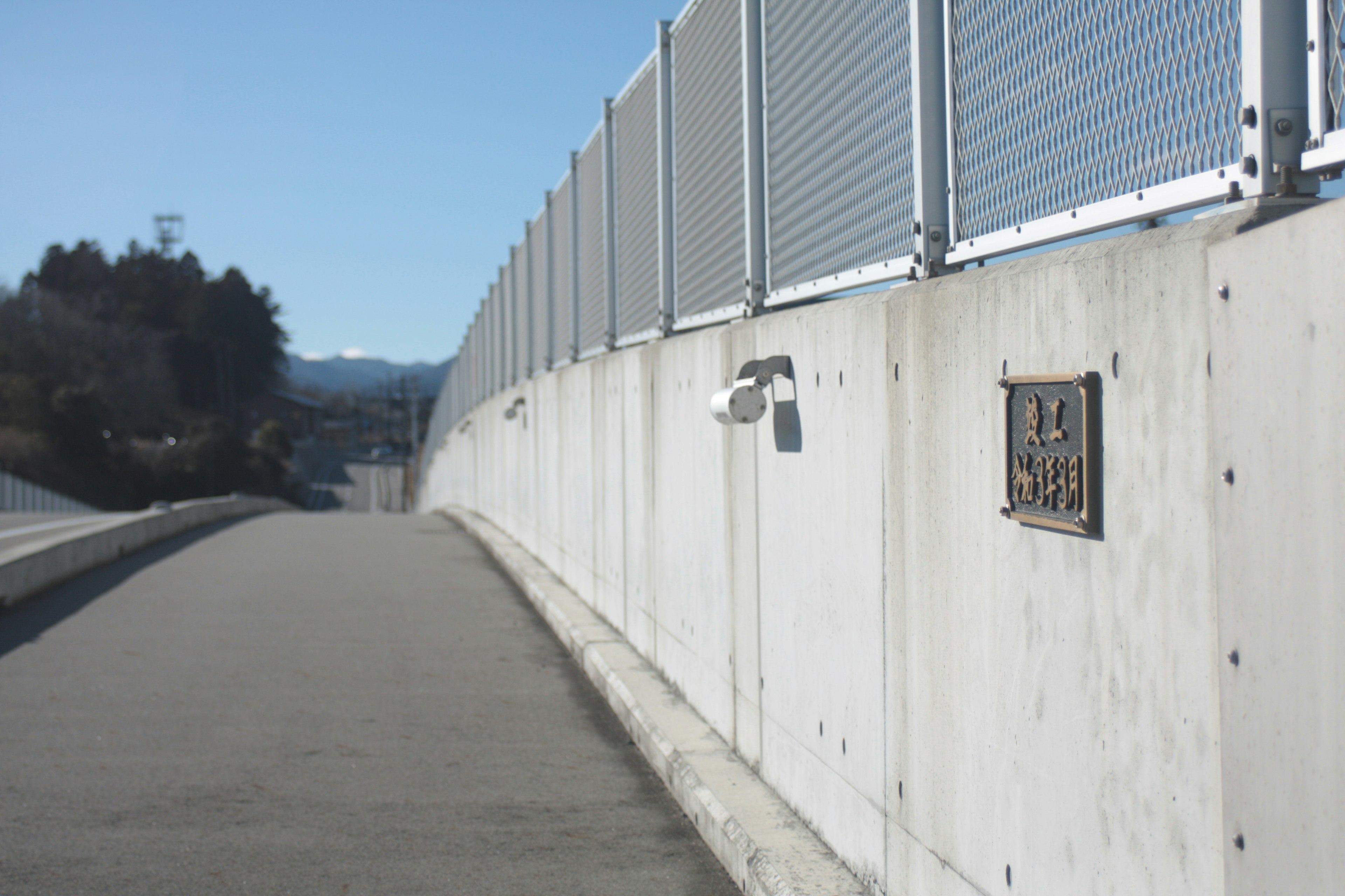 A view of a sidewalk with a concrete wall and a fence