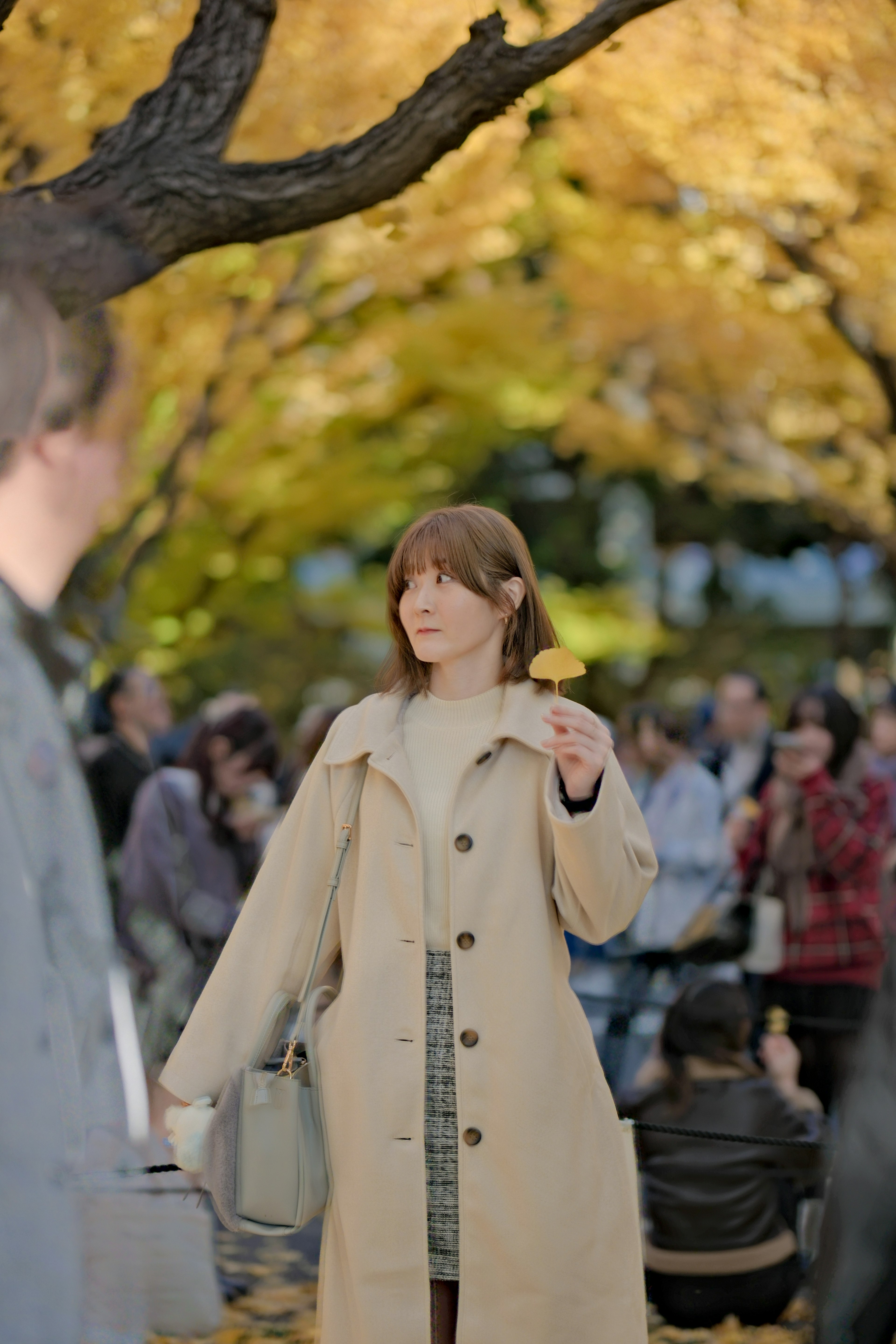 Una donna in un cappotto beige che si trova in mezzo a una folla in un parco autunnale