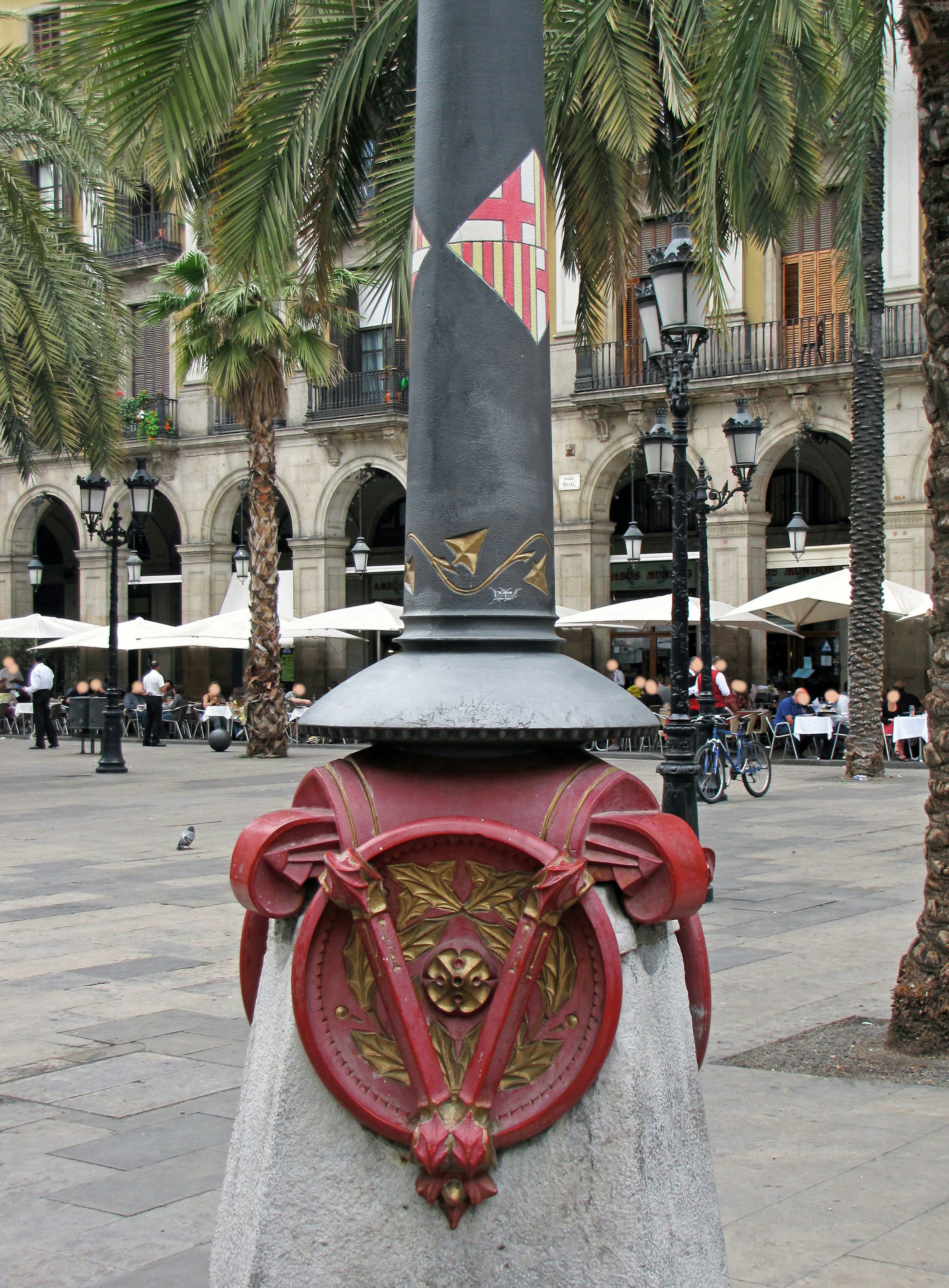 Base de farola decorativa en una plaza de Barcelona con diseño de escudo rojo