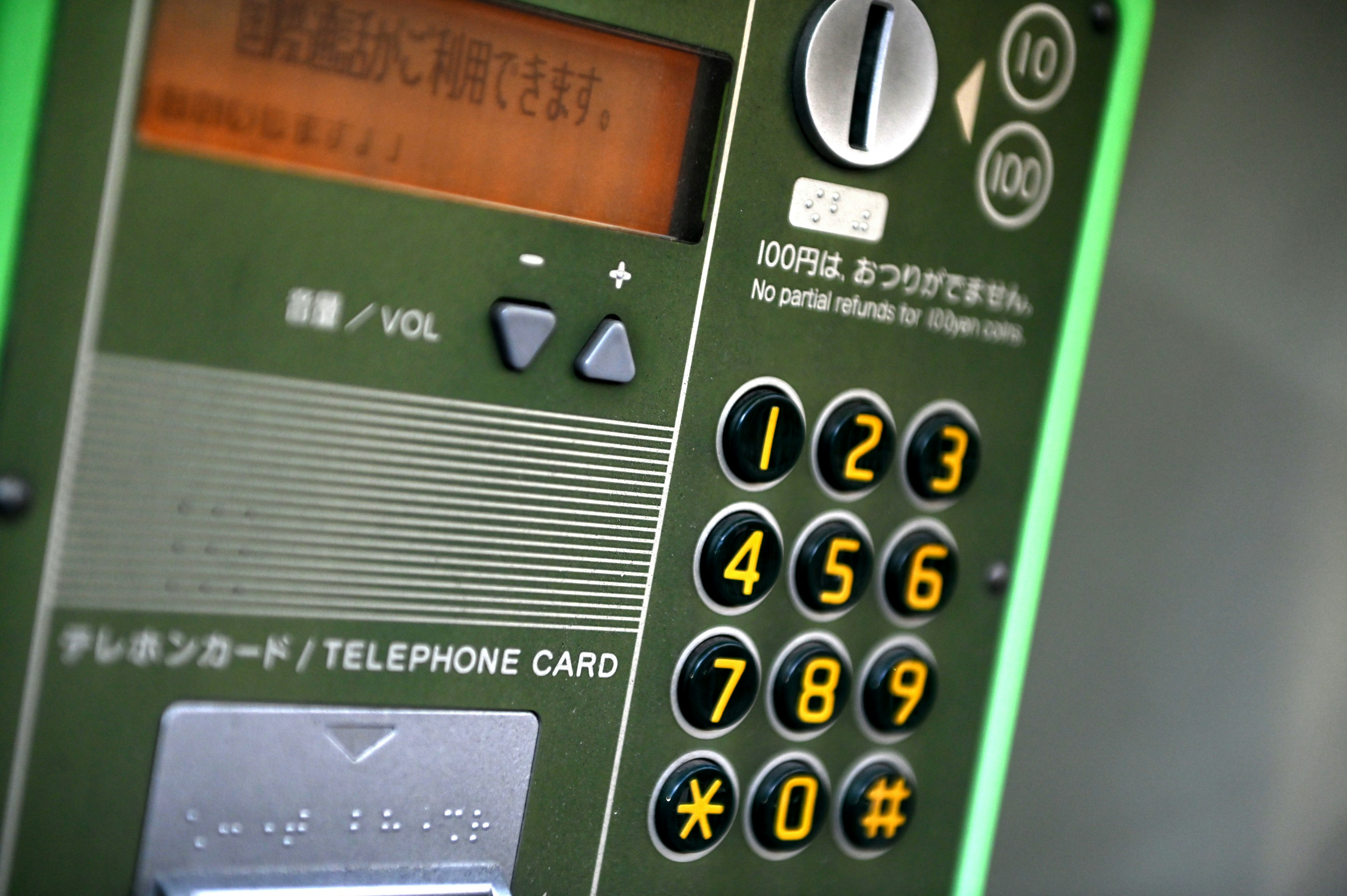 Close-up of a green public telephone with numeric buttons and a telephone card slot