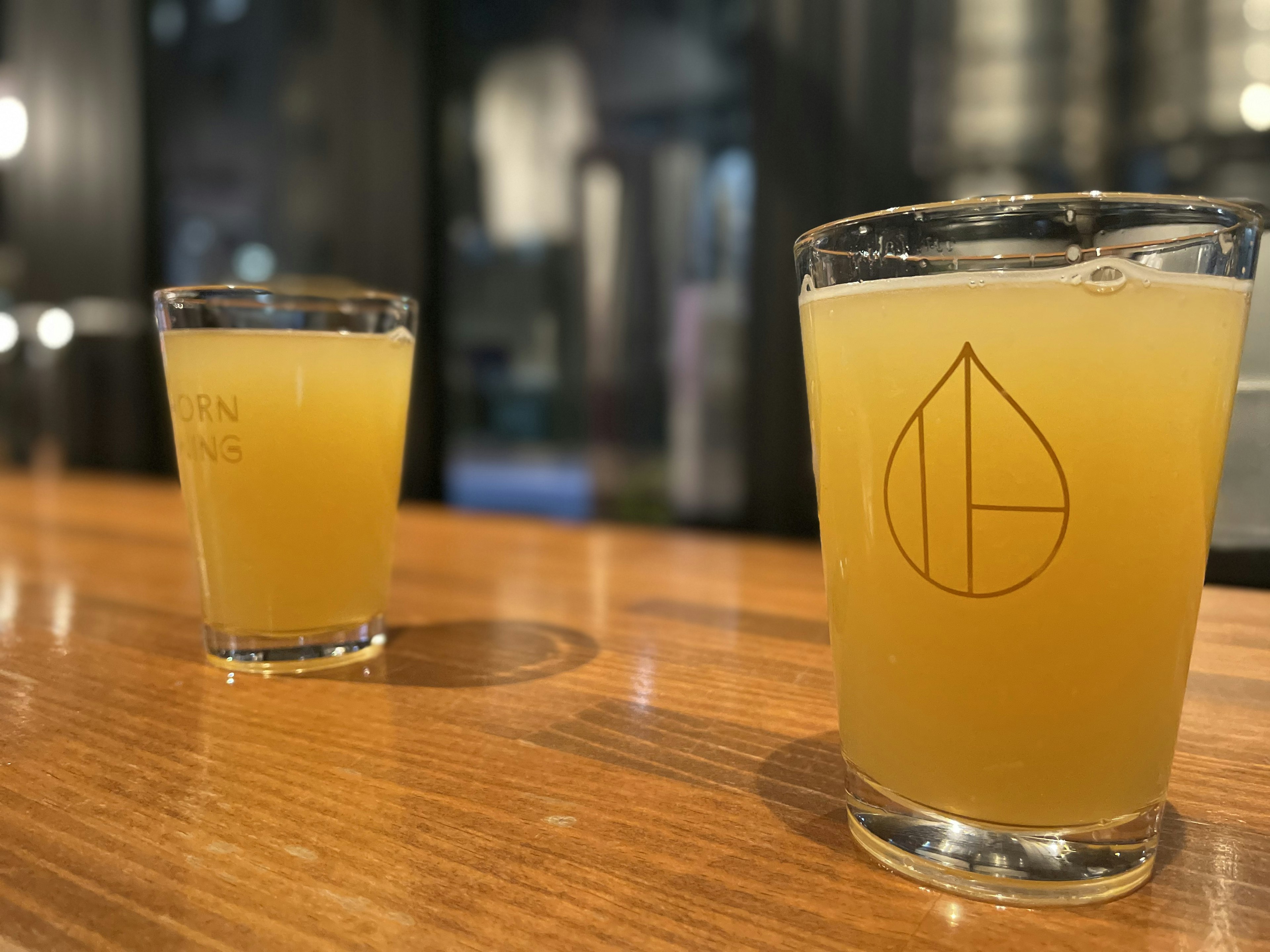 Two glasses of yellow drink on a wooden table with a logo on one glass