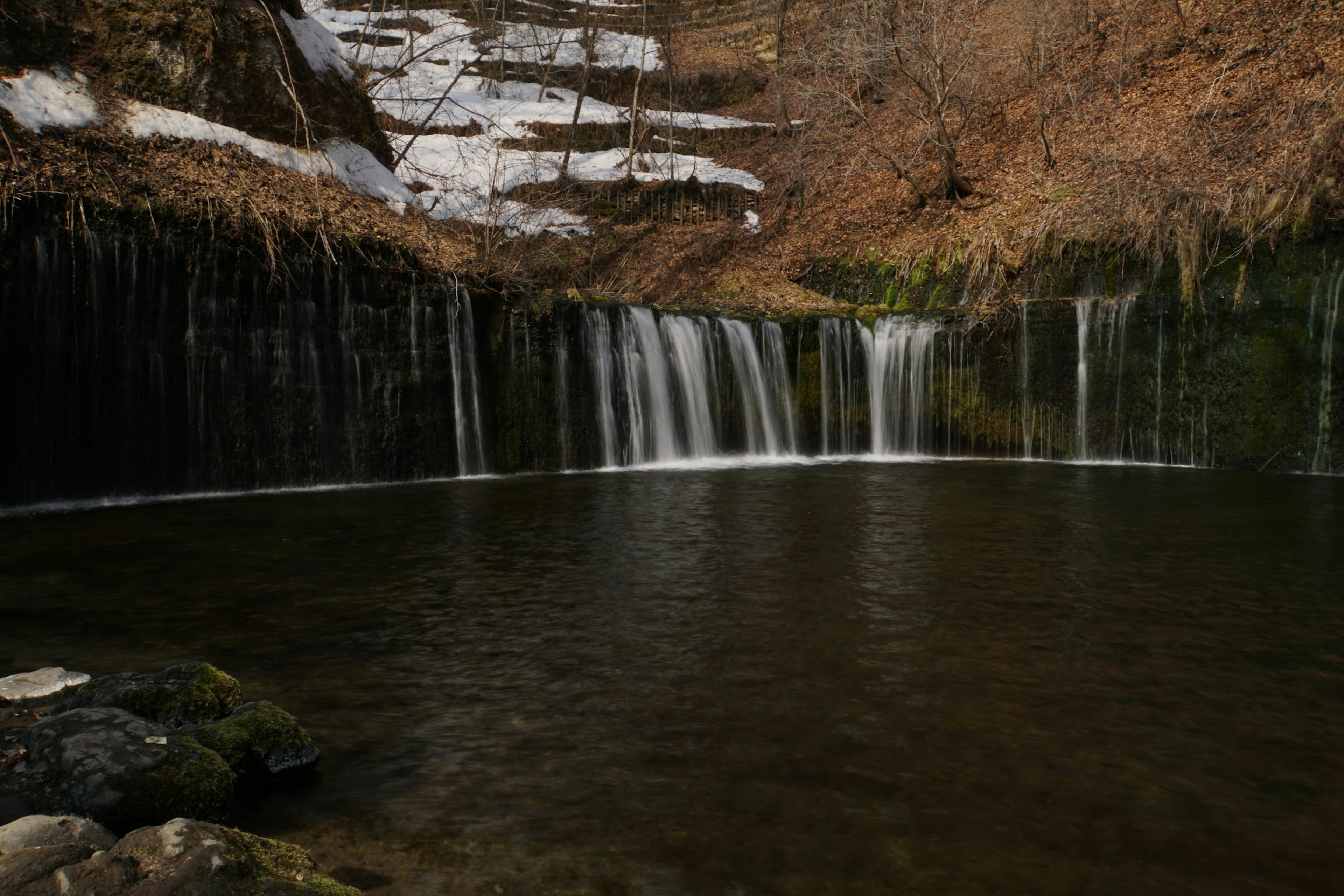 Scenic view of a waterfall flowing into a tranquil pond surrounded by bare trees