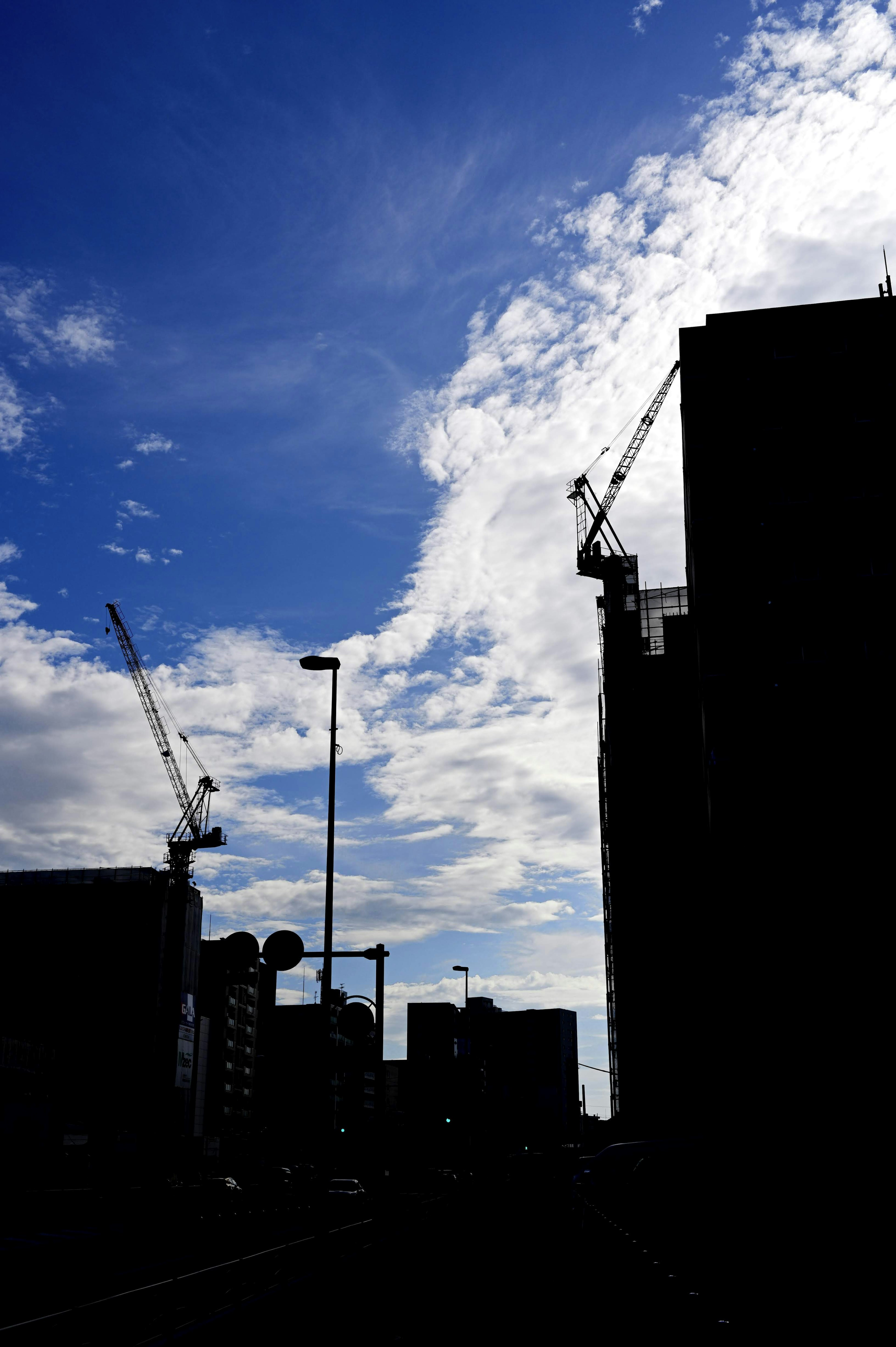 青空の下での建設現場のシルエットクレーンとビルが見える